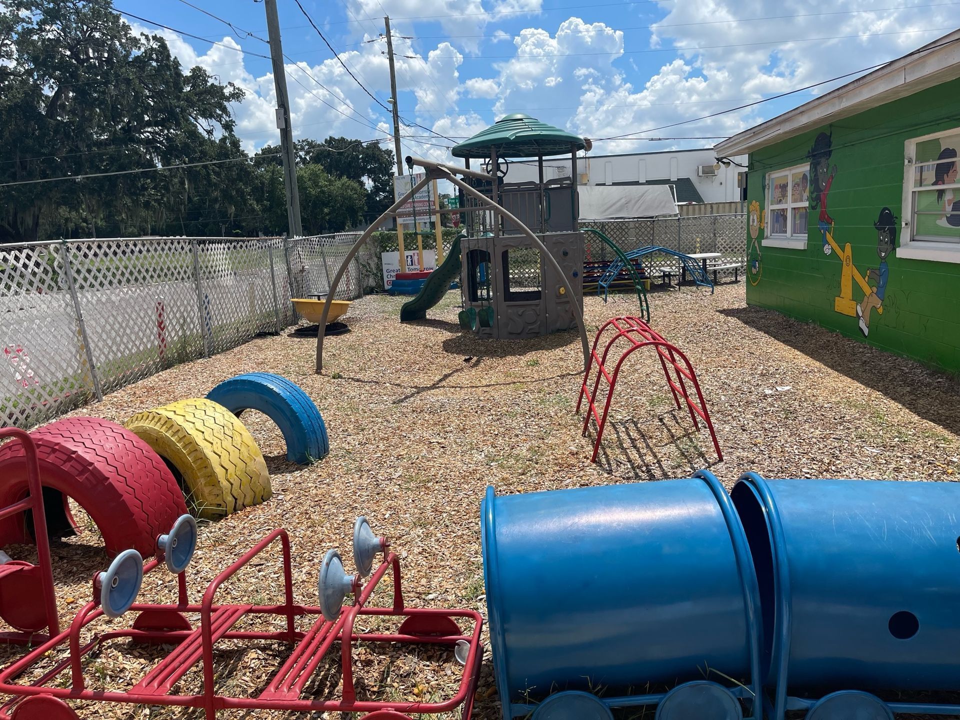 A playground with a train and a slide in front of a green building.
