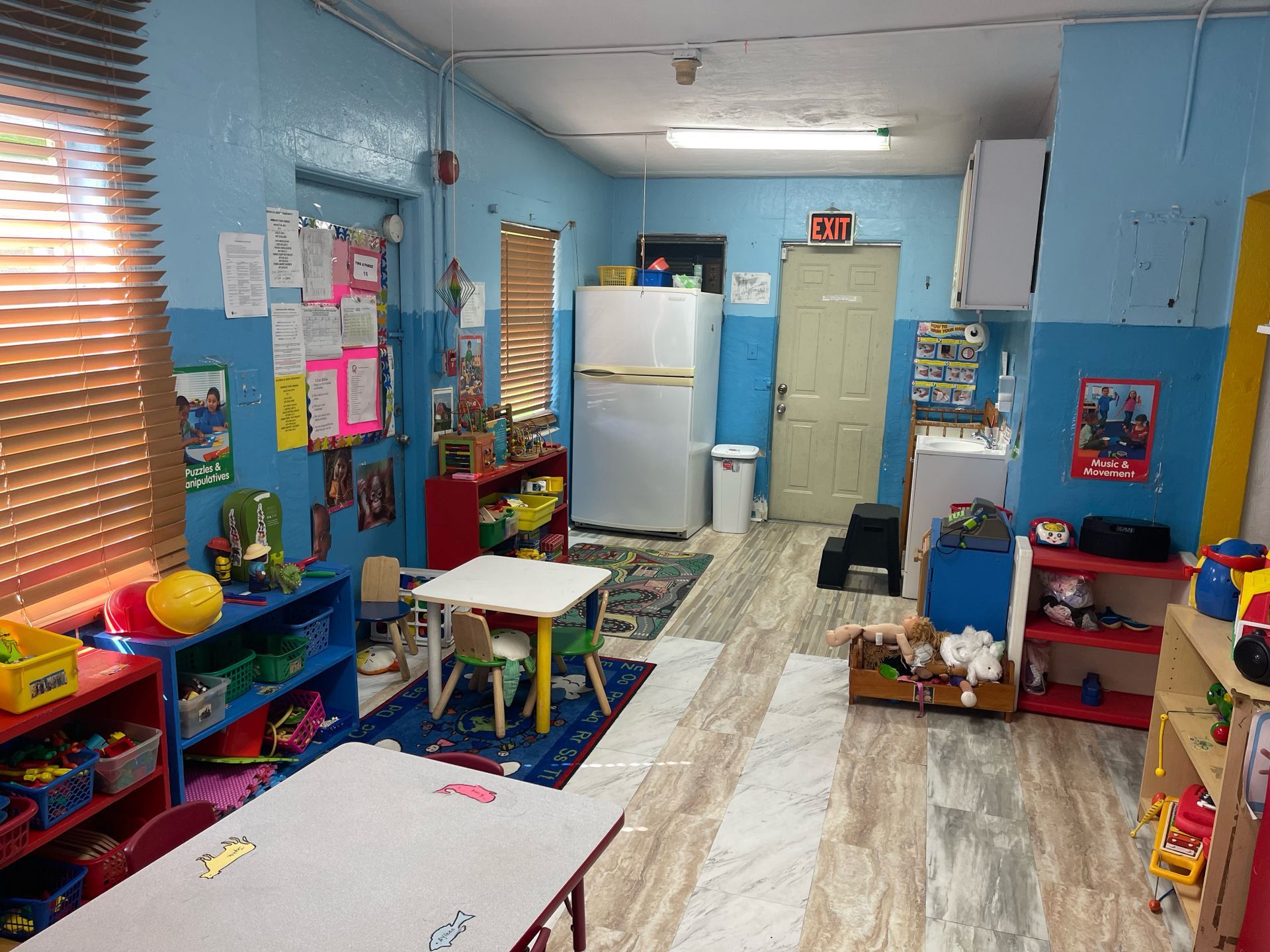 A classroom with tables , chairs , shelves and a refrigerator.