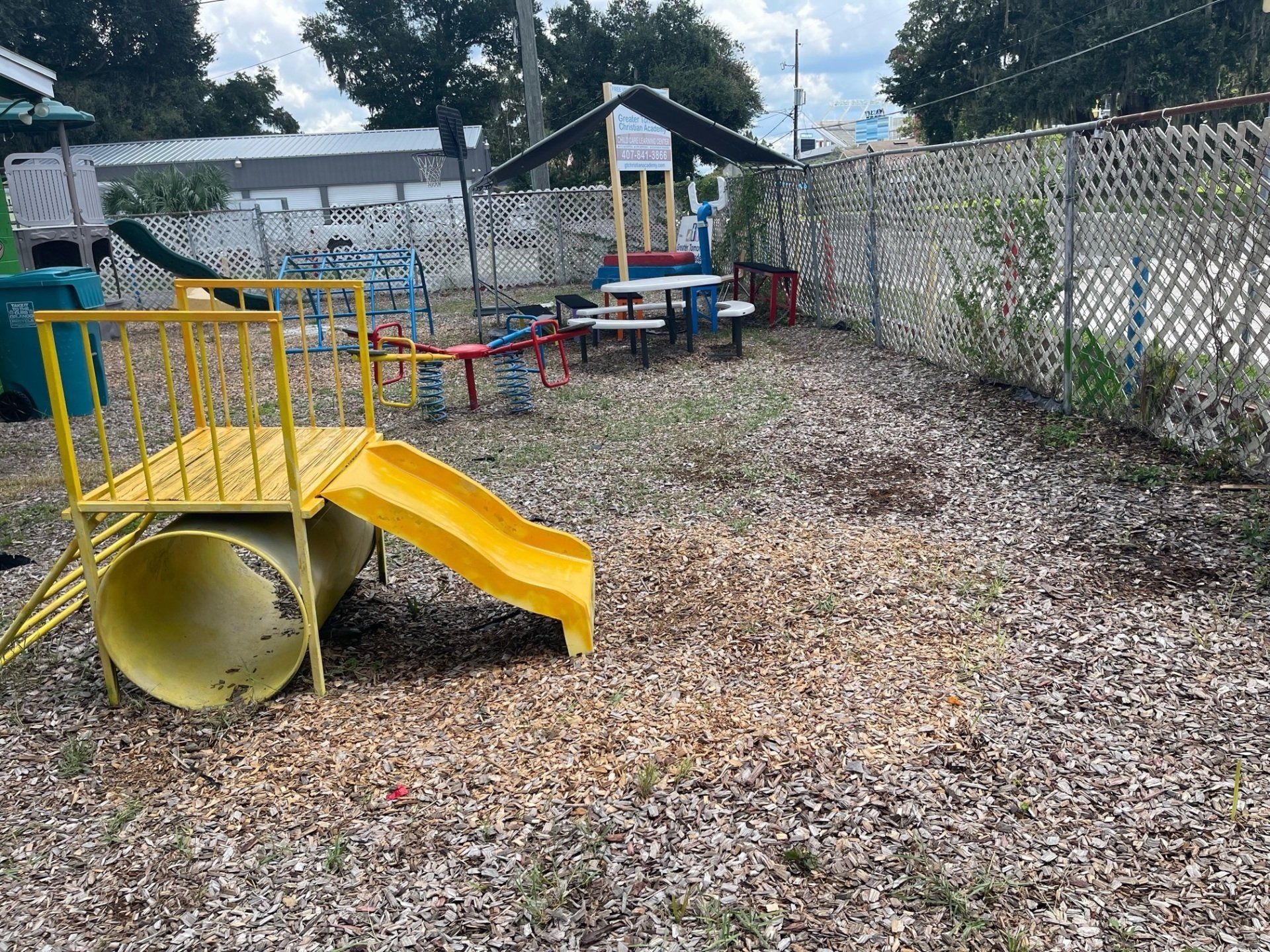 A playground with a yellow slide , tunnel , and benches.