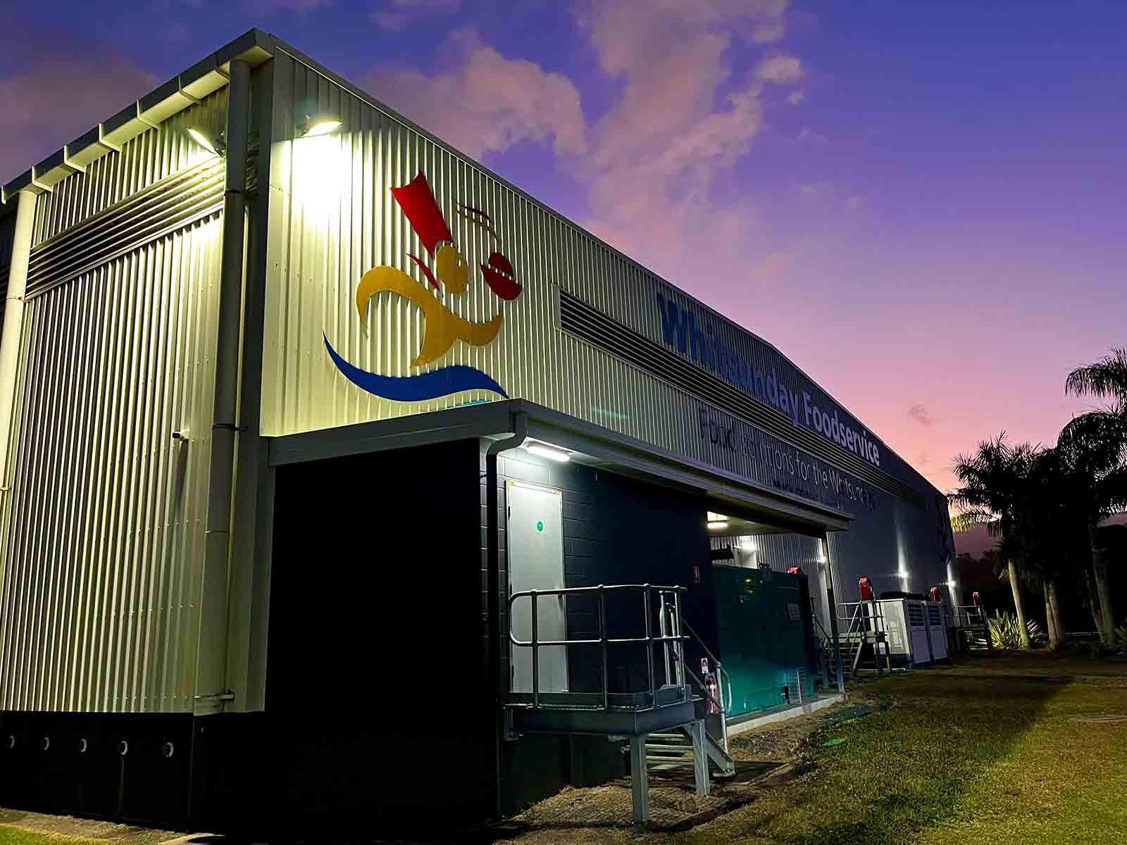 A Large Building With A Painting On The Side Of It Is Lit Up At Night — IPOWER Industries In Cannonvale, QLD