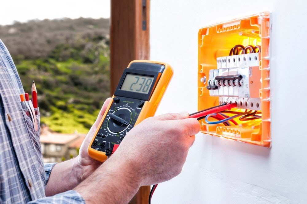 A Man Is Using A Digital Multimeter To Test An Electrical Box — IPOWER Industries In Bowen, QLD