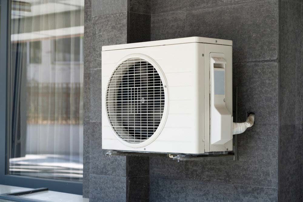 A White Air Conditioner Is Mounted On The Side Of A Building Next To A Window — IPOWER Industries In Bowen, QLD
