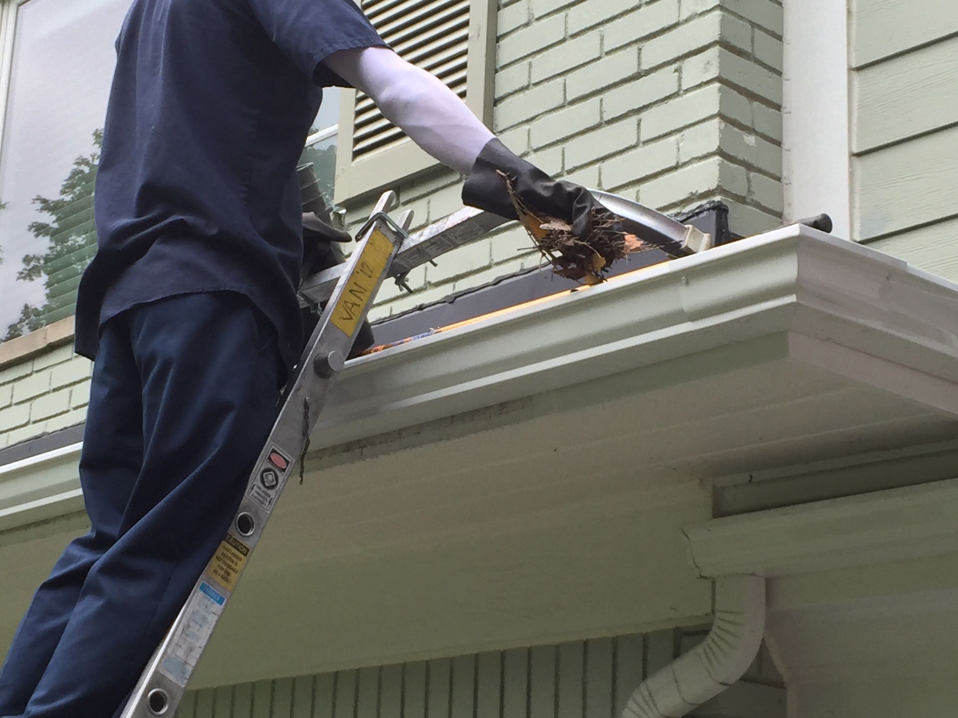 A man is standing on a ladder fixing a gutter on a house.