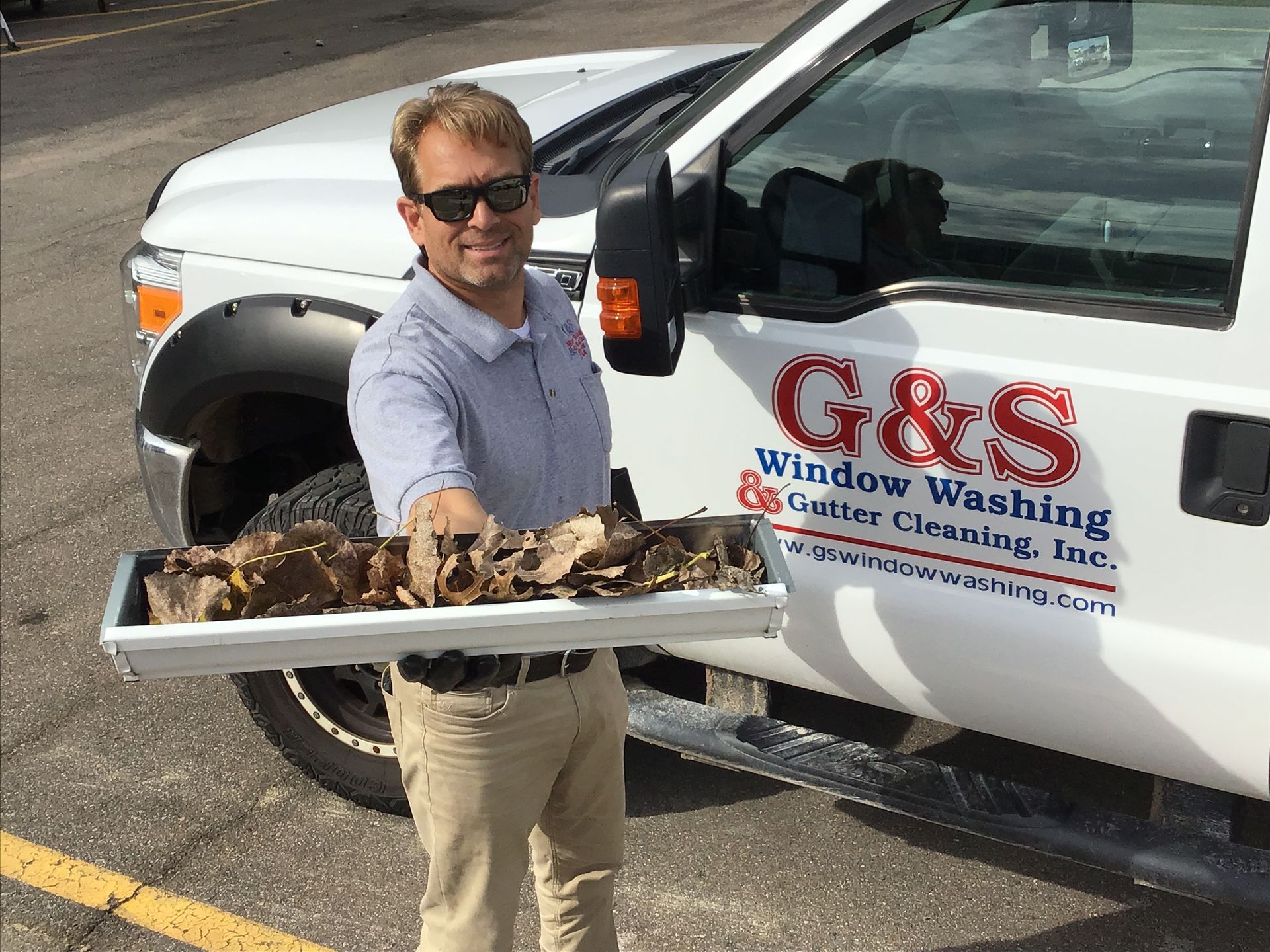 A man is holding a tray of leaves in front of a g & s window washing truck
