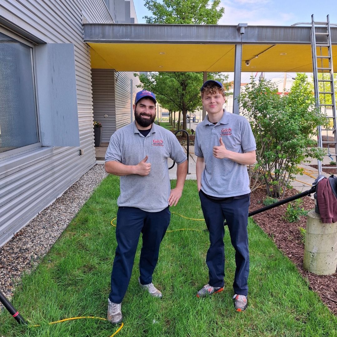Two men are standing in the grass giving a thumbs up.