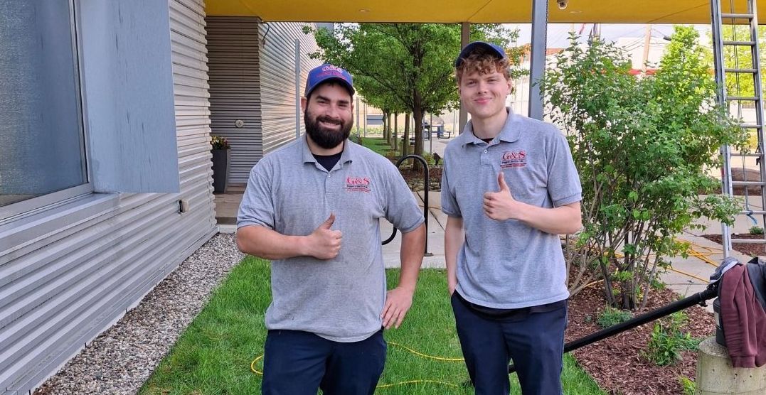 Two men are standing in the grass giving a thumbs up.