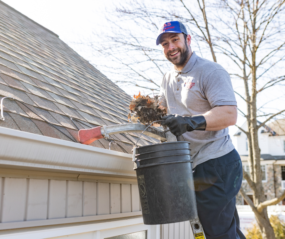 A man is cleaning the gutters of a house with a bucket.
