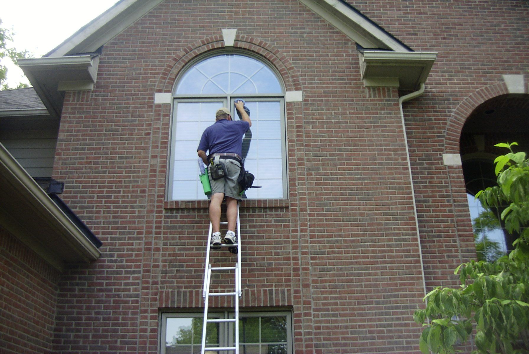 A man on a ladder cleaning a window on a brick building