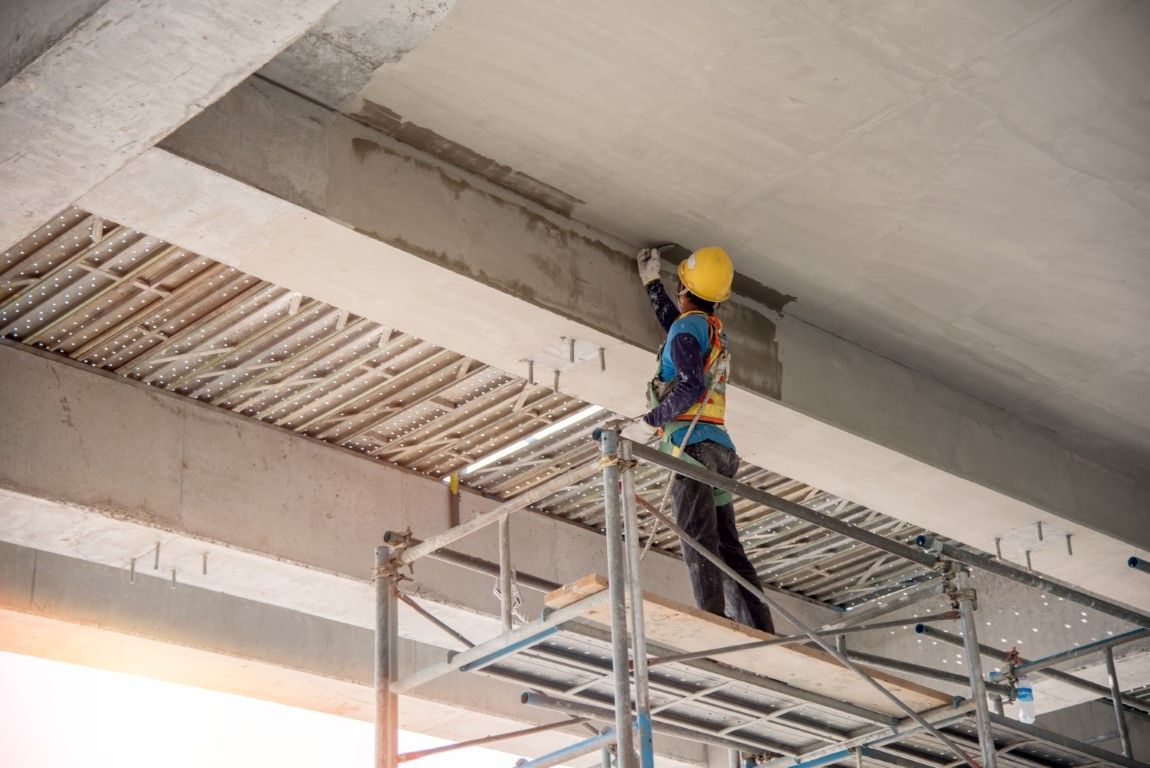 Worker on a scaffold inspecting the ceiling of a building under construction