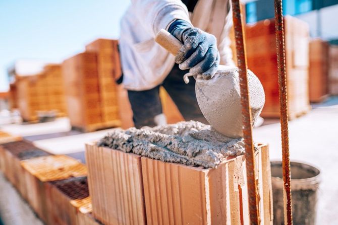 Construction worker pouring wet concrete into a cinder block wall frame at a building site