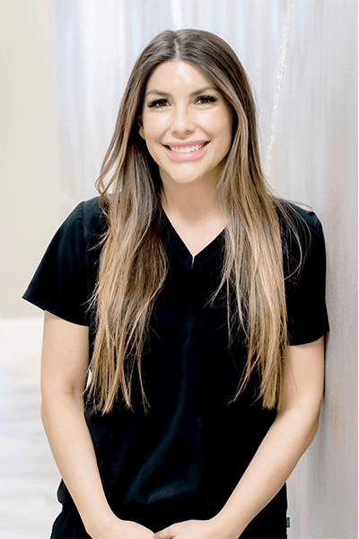 A woman with long hair is wearing a black scrub top and smiling.