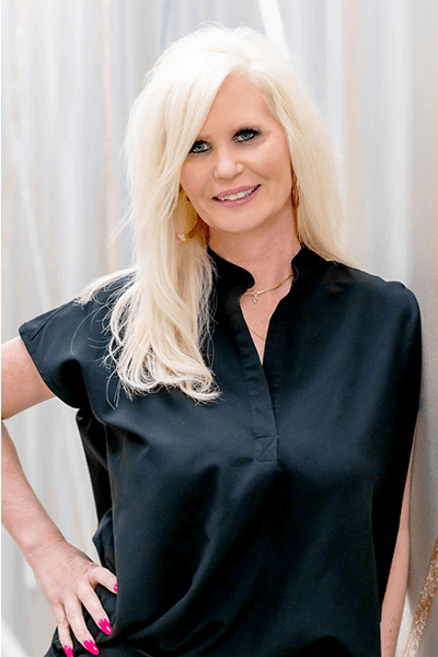 A woman with blonde hair is wearing a black shirt and smiling.