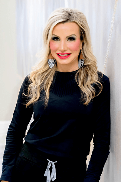 A woman wearing a black sweater and earrings is standing in front of a white curtain.
