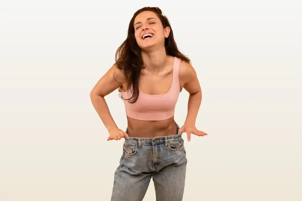 A woman in a pink crop top and jeans is laughing.