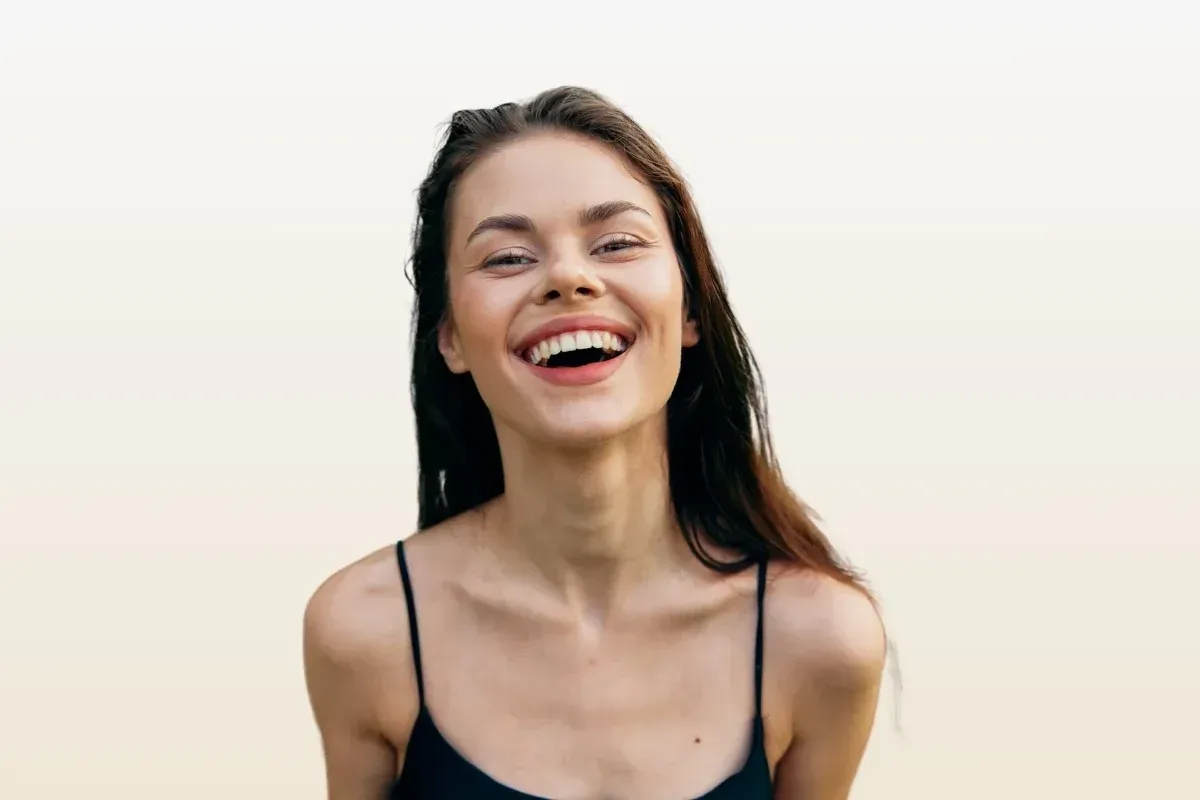 A woman in a black tank top is laughing with her mouth open.