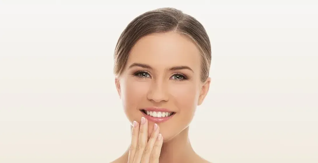 A woman is smiling and touching her face with her hand.