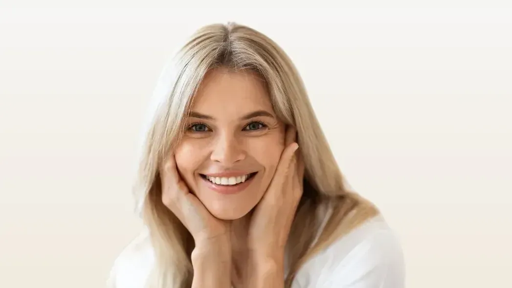 A woman is smiling with her hands on her face.