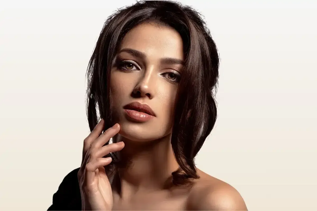 A woman is touching her face with her hand and looking at the camera.