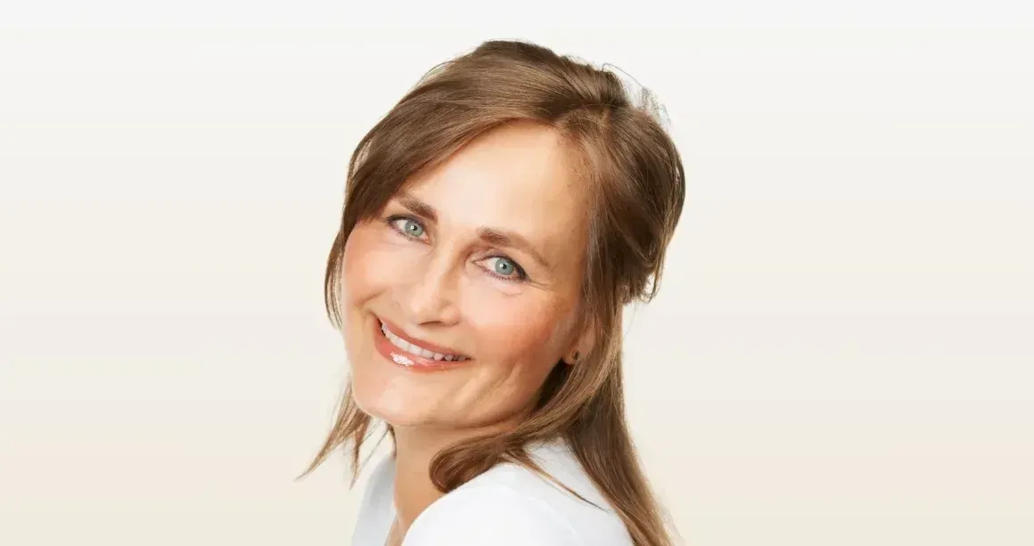 A woman in a white shirt is smiling and looking at the camera.