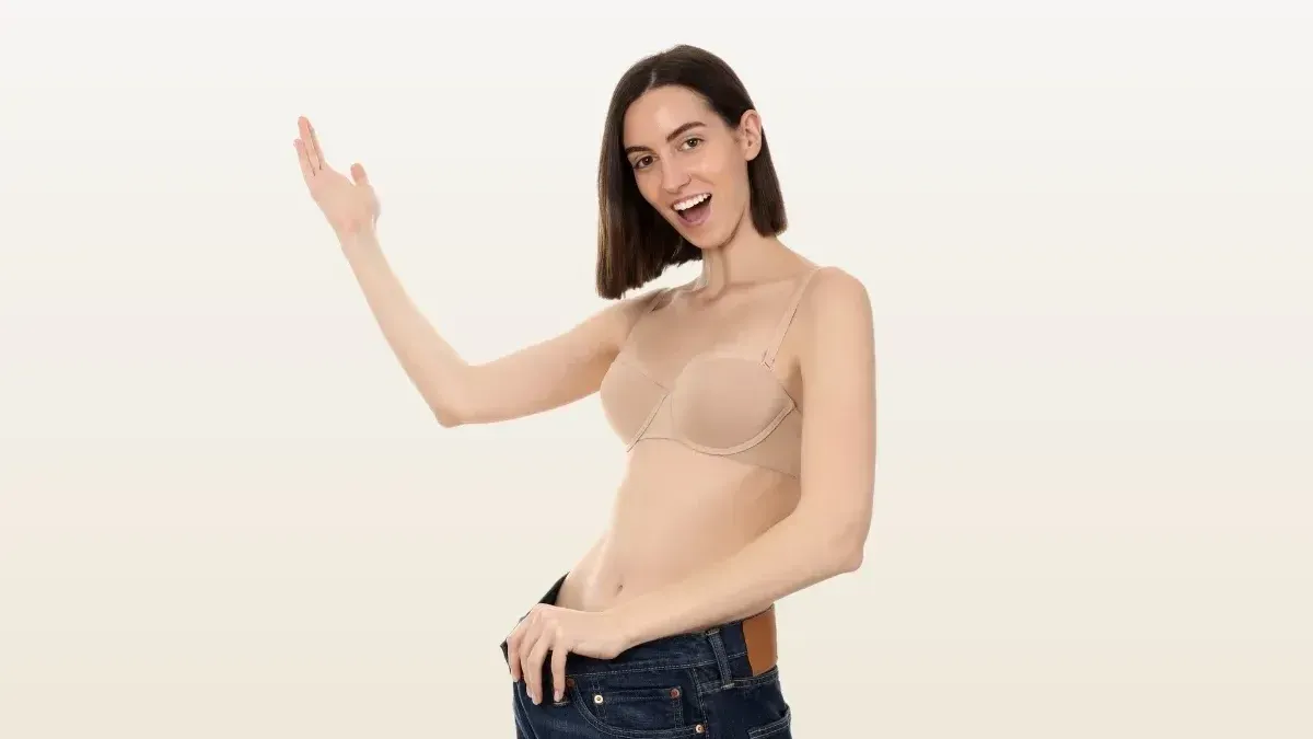 A young woman in a tank top and jeans is holding her jeans out from her waist and is excited