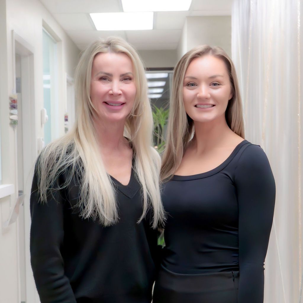 Two women are standing next to each other in a hallway and smiling for the camera.