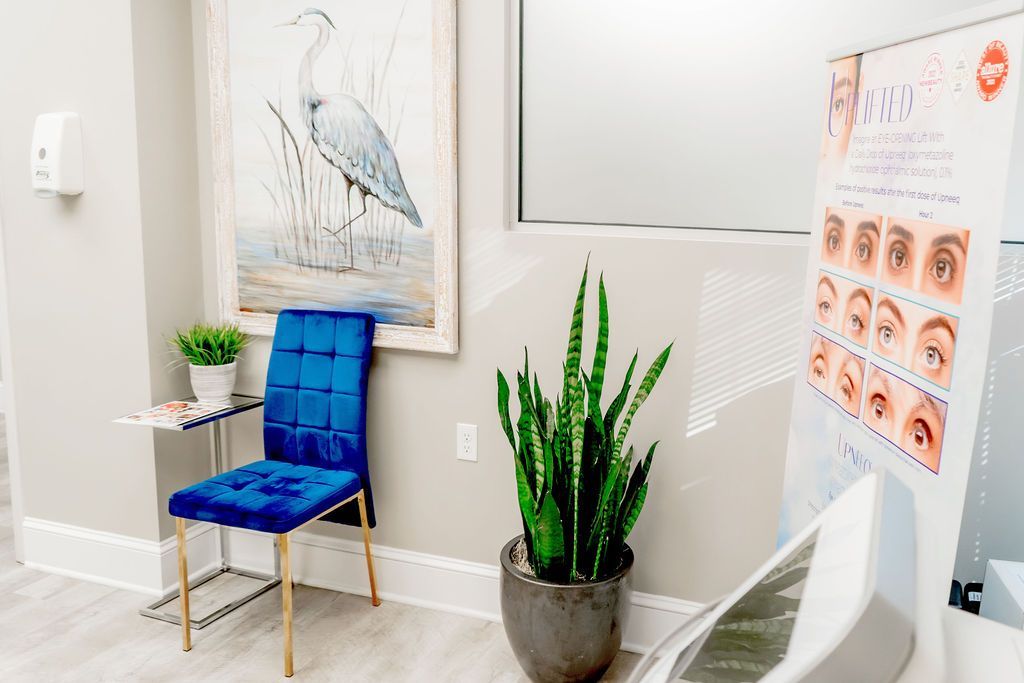 A waiting room with a chair , potted plant , and a painting on the wall.