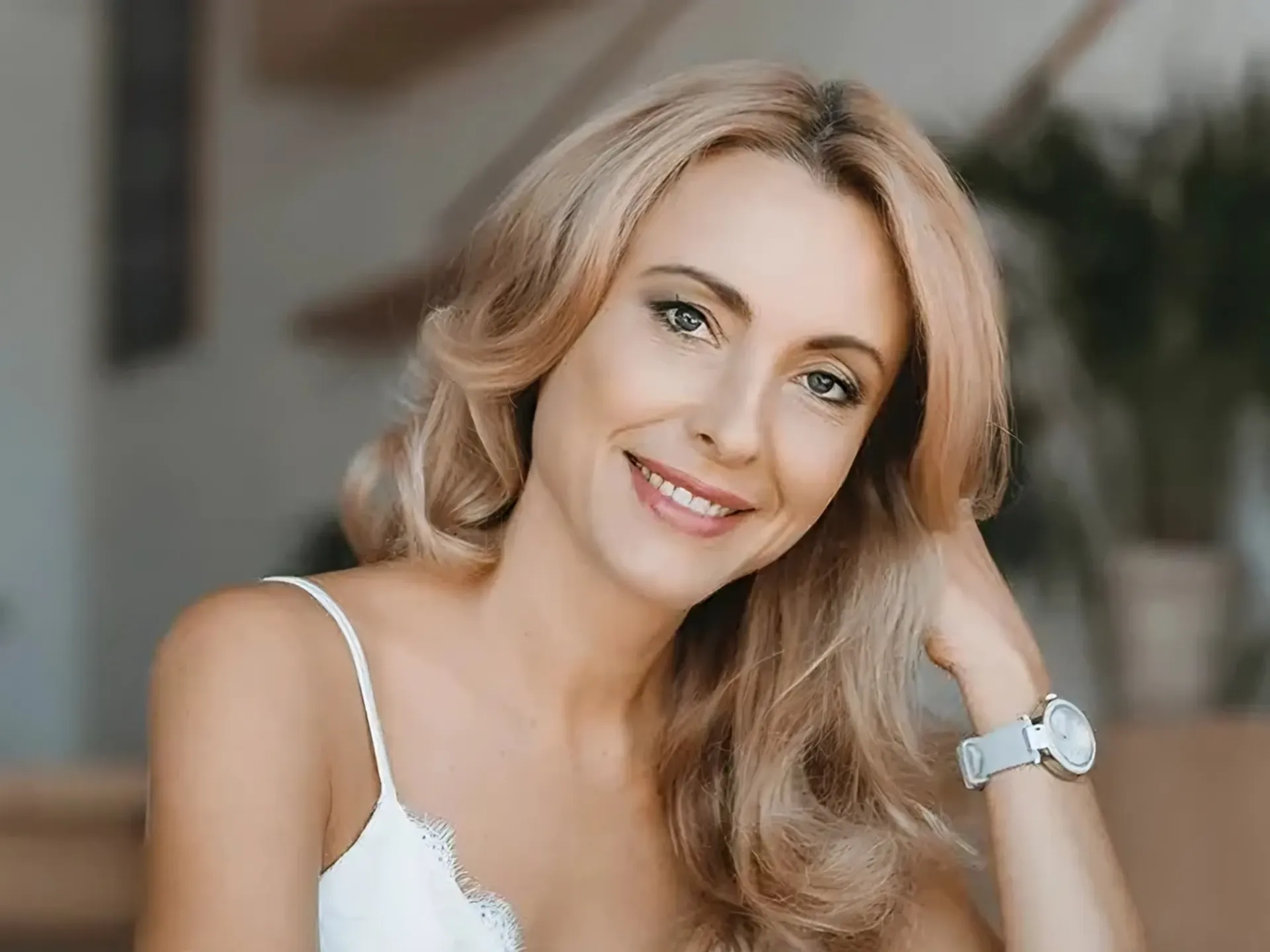 A woman wearing a white tank top and a watch is smiling.