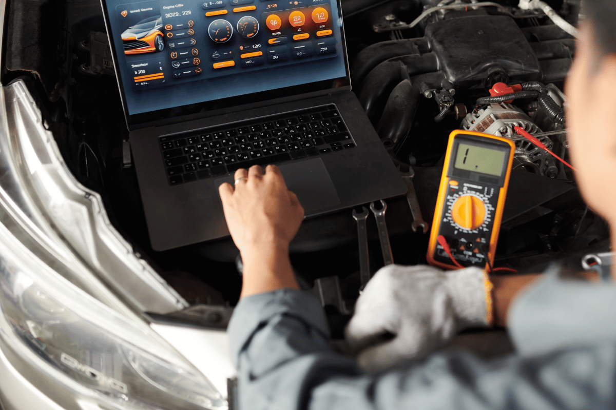 Mechanic using a laptop and multimeter to diagnose a car engine in a garage
