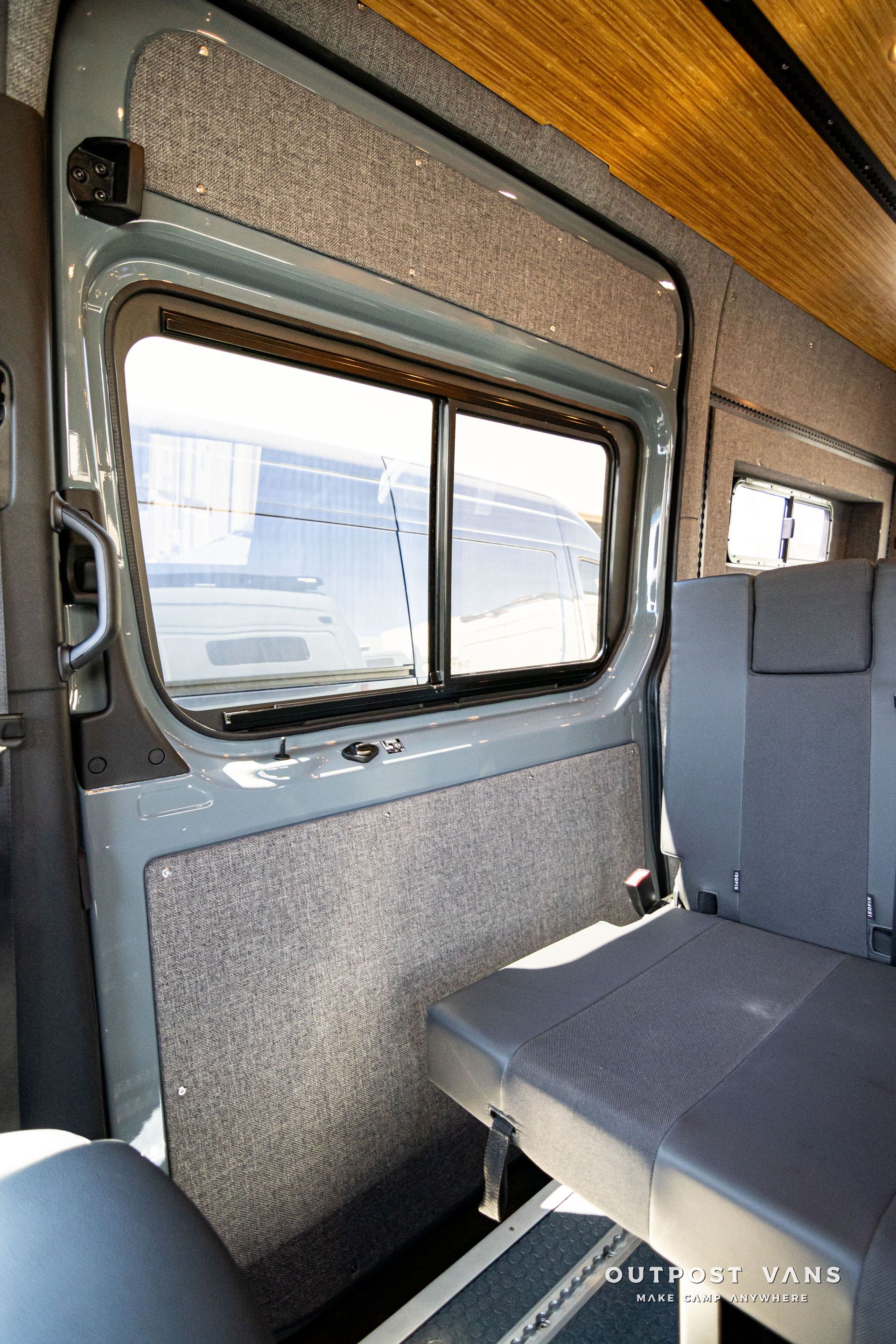 The back seat of a van with a bed and a window.