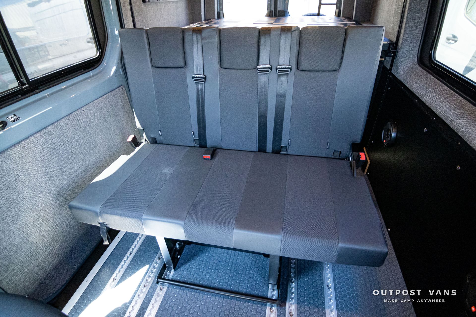 The back seat of a van with seat belts on it.