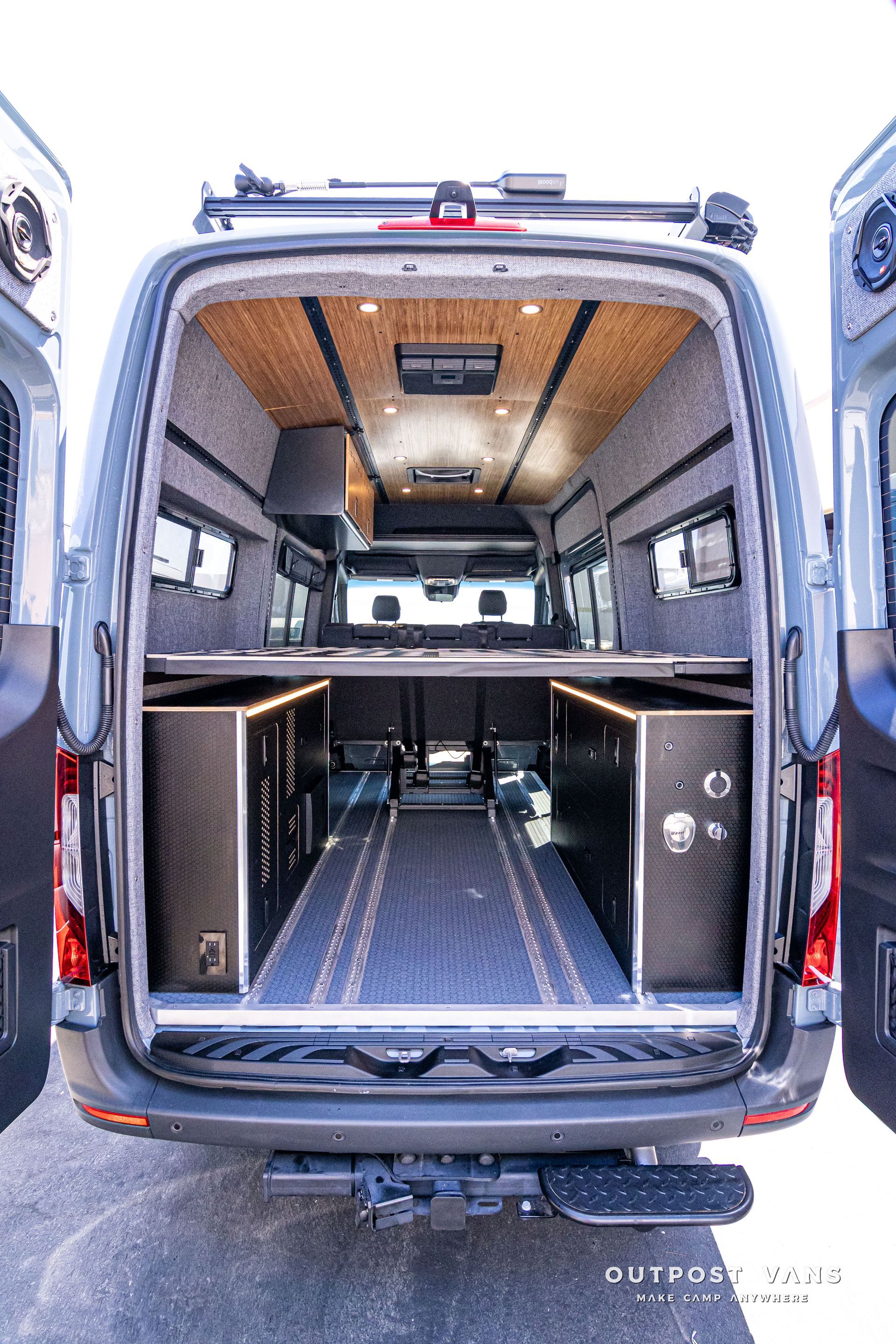 The back of a van with the door open and a bed in the back.