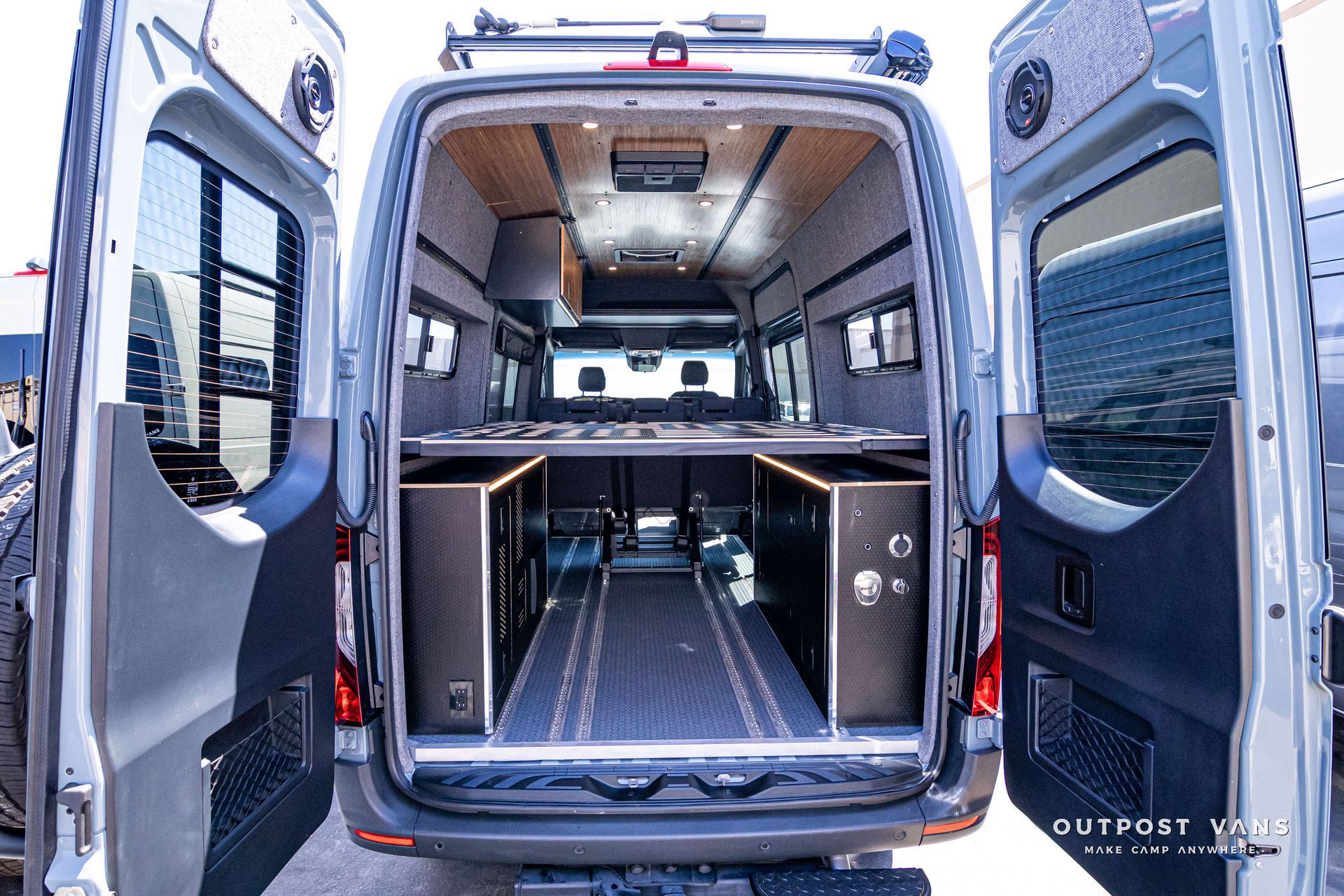 The back of a van with its doors open and a bed in the back.