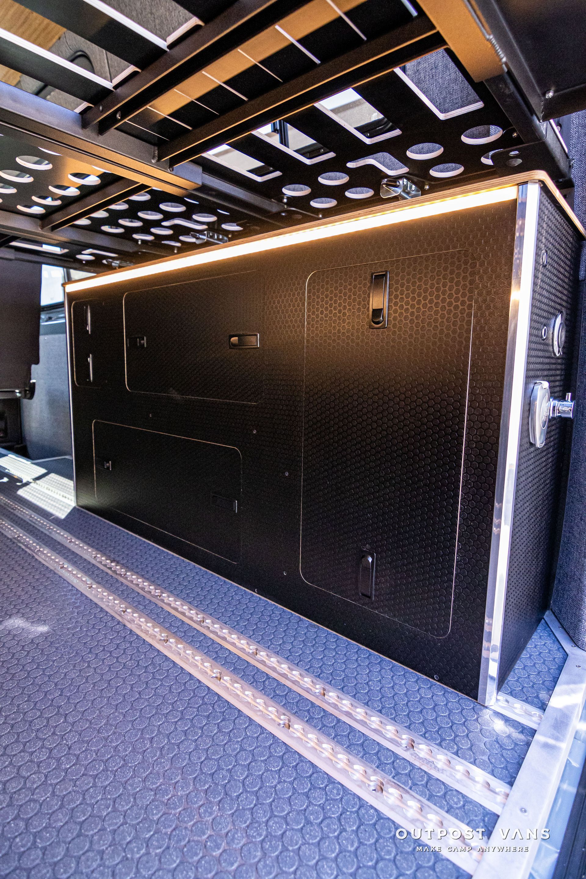 A large black box is sitting under a bed in a van.