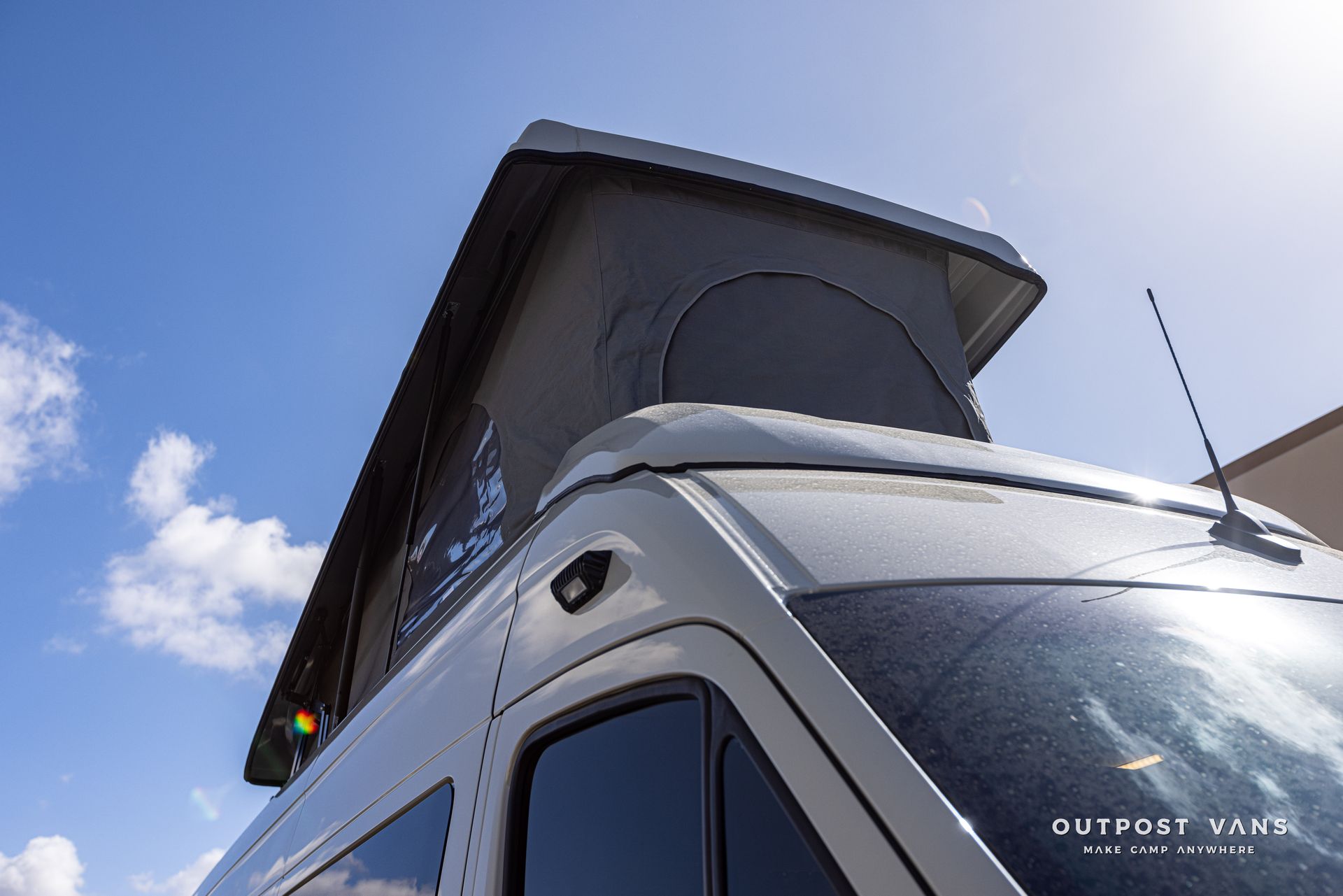 A van with a pop up roof is parked in front of a blue sky.