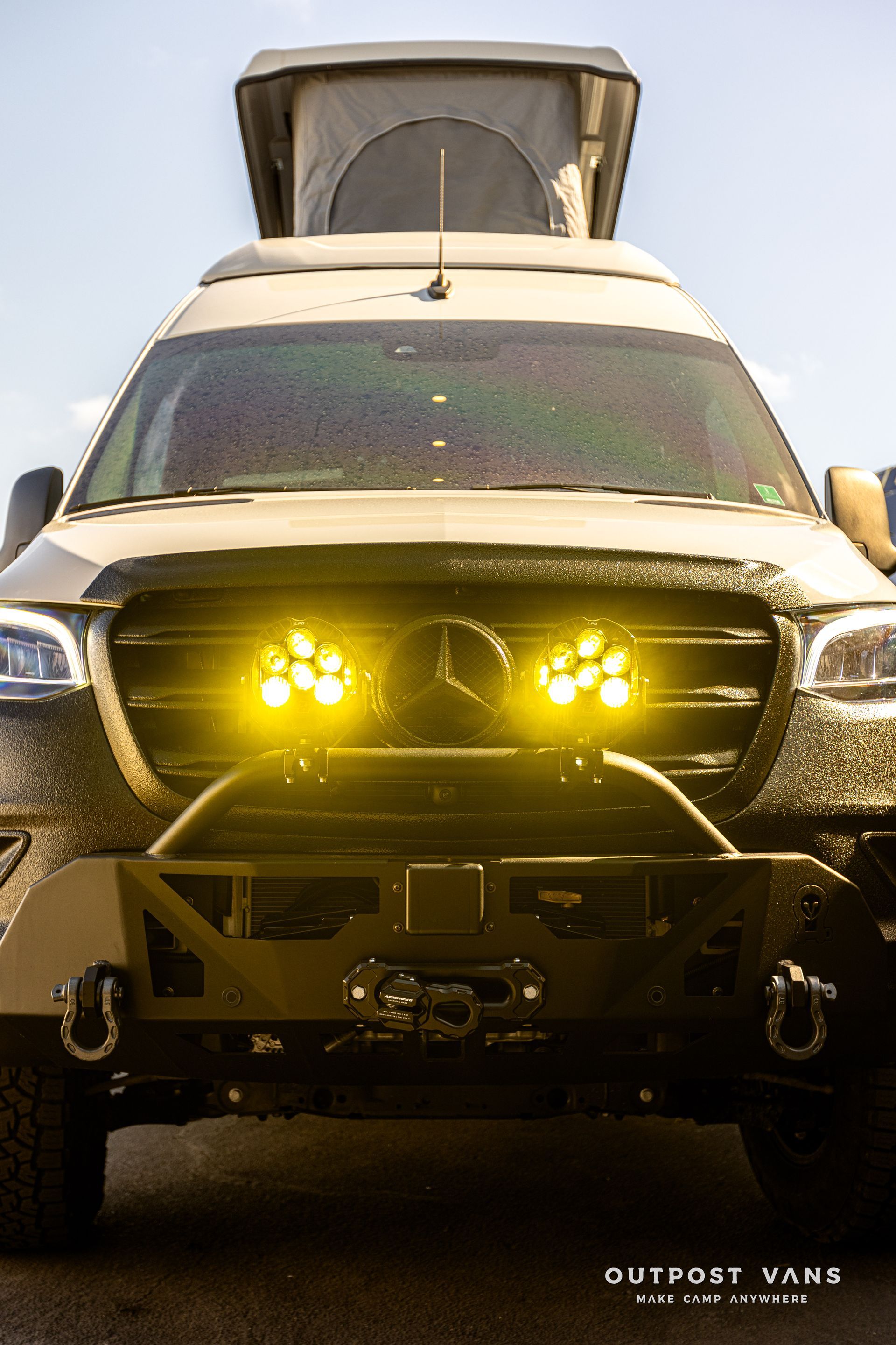 A mercedes sprinter van with a pop up roof is parked on the side of the road.