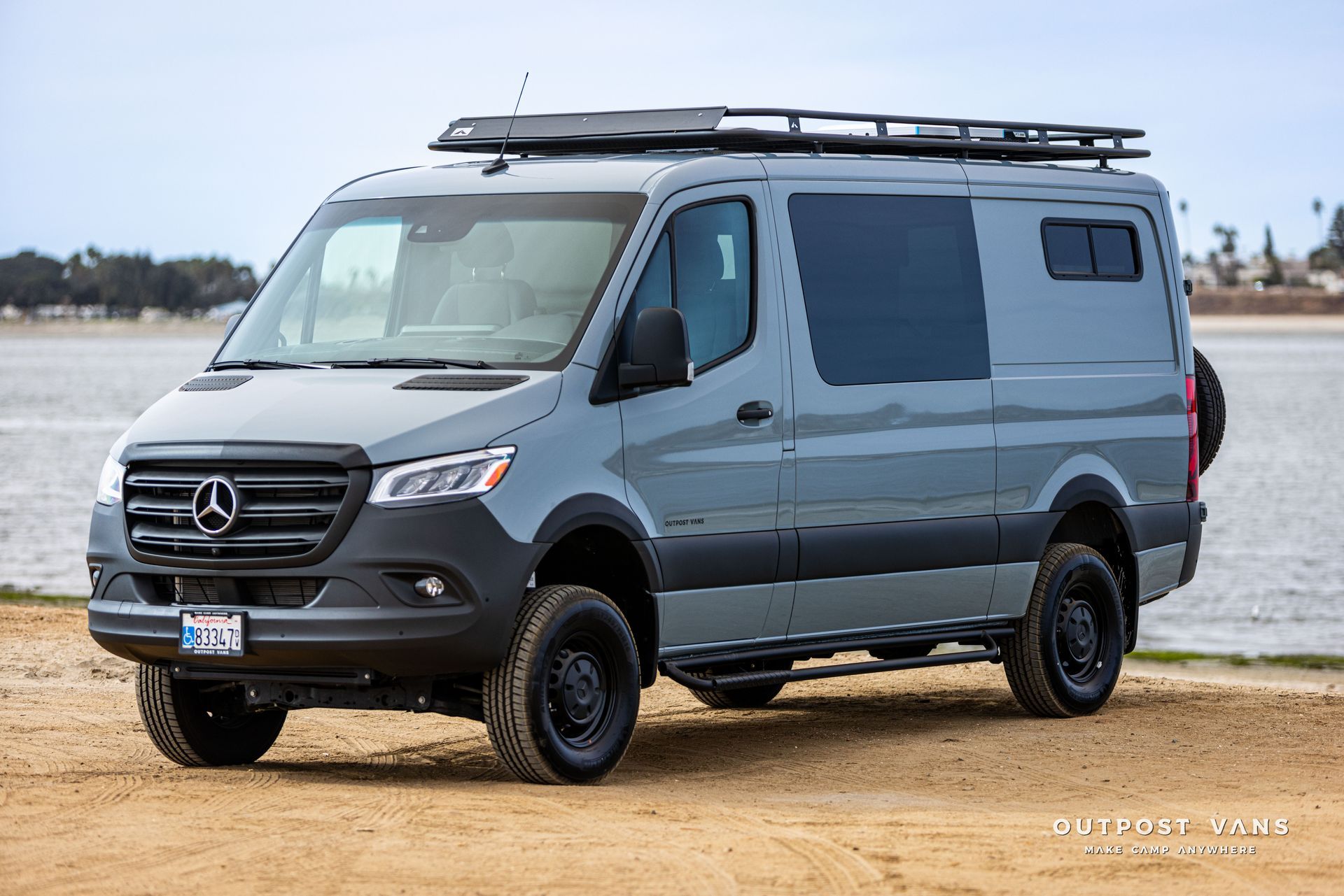 A mercedes sprinter van is parked on the beach next to a body of water.