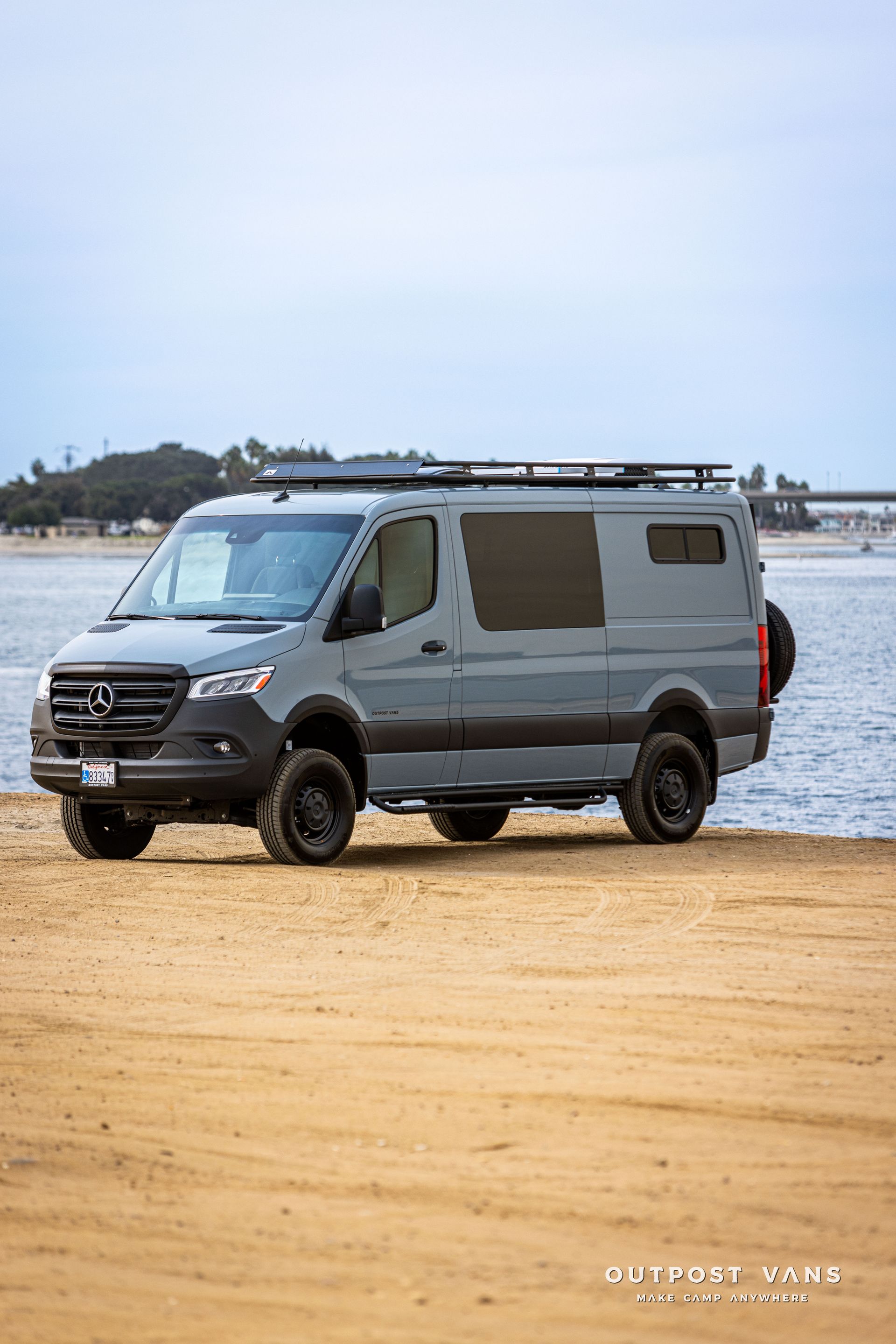 A van is parked on a sandy beach next to a body of water.