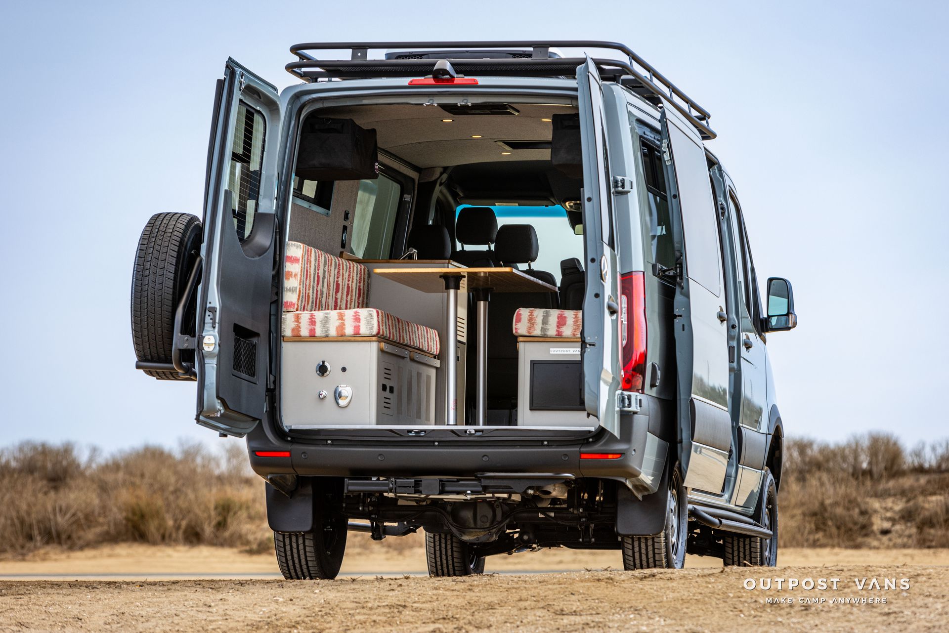 The back of a van with its doors open is parked in the desert.