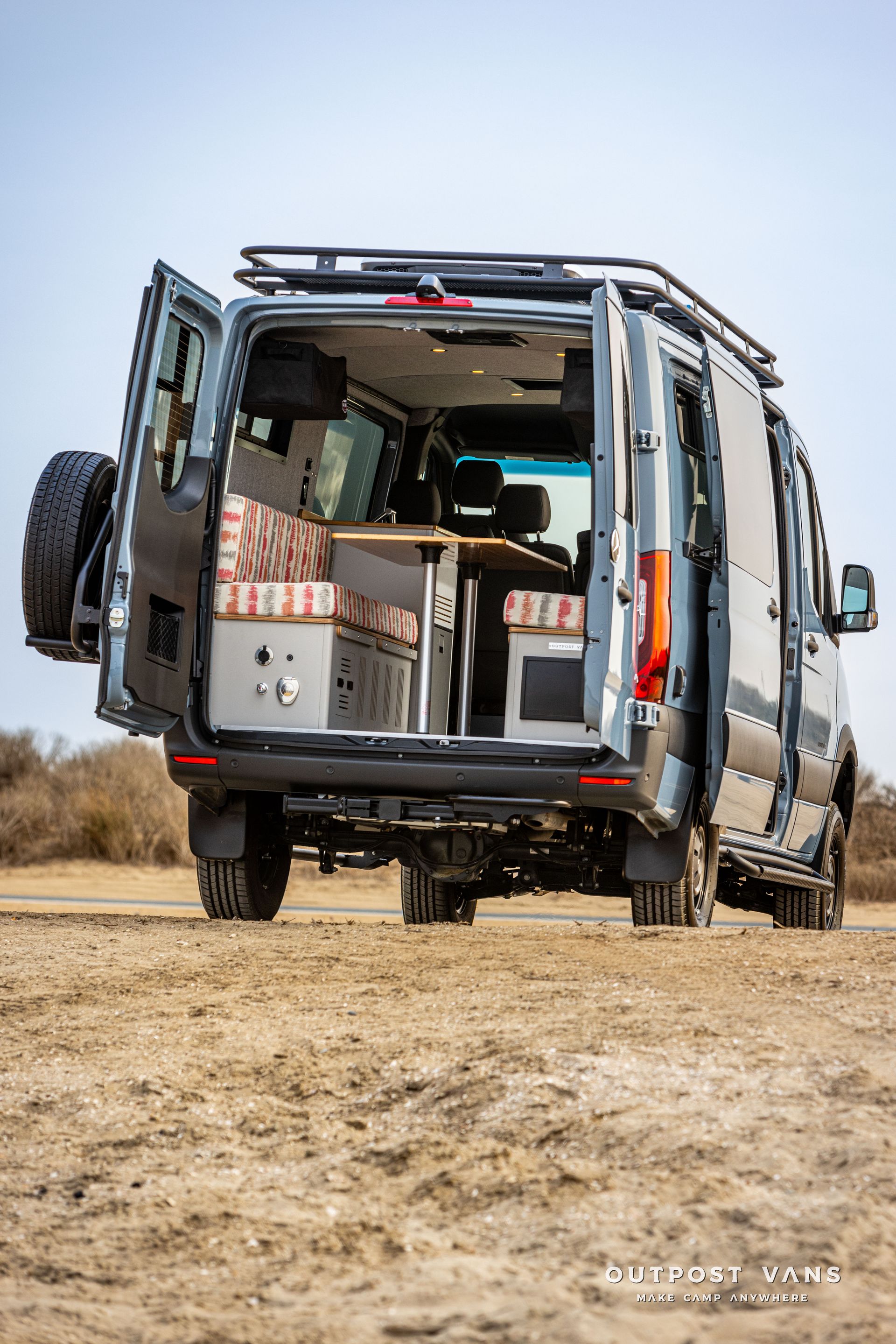 A van is parked in the dirt with its doors open.