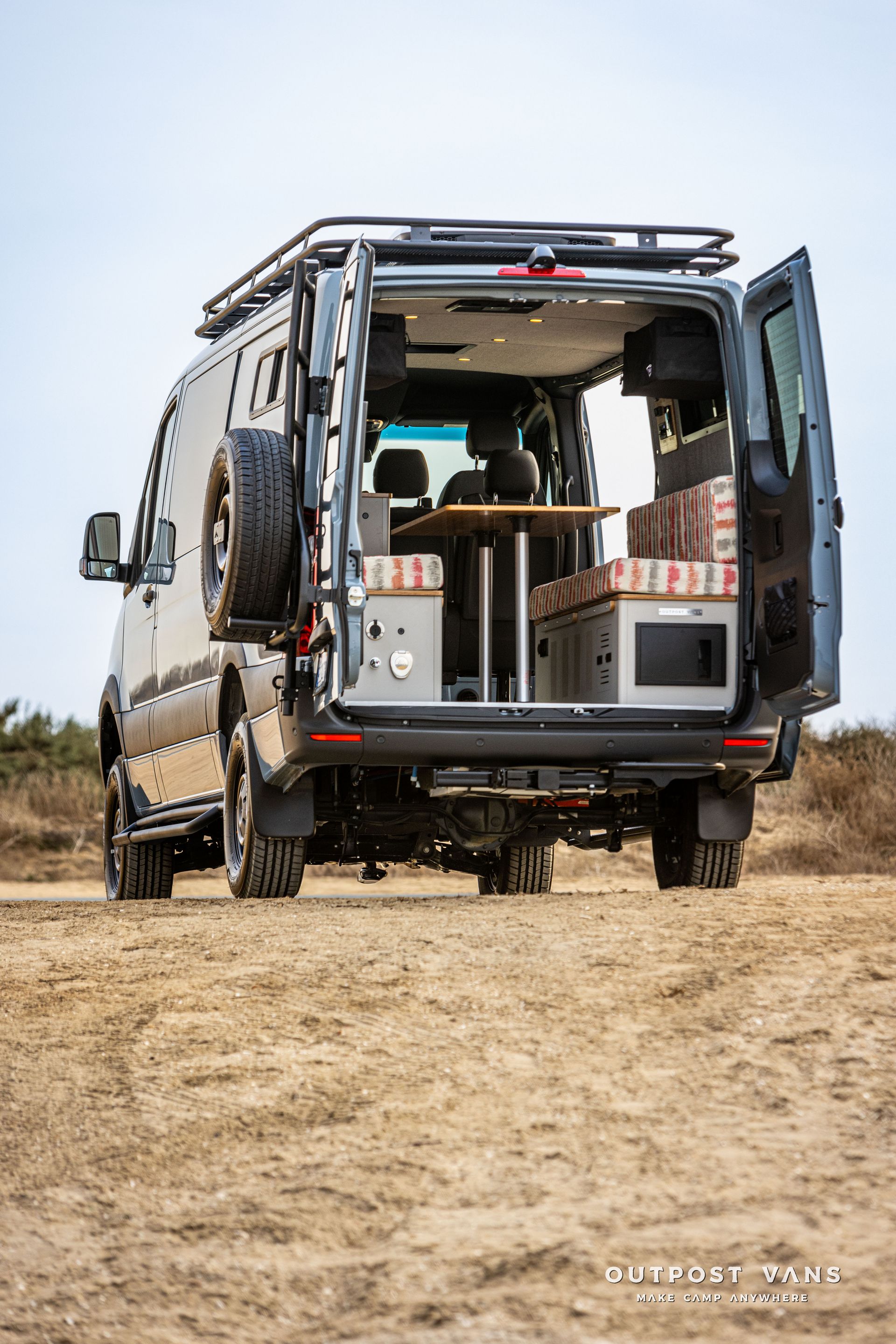 A van is parked in the middle of a dirt field with its doors open.