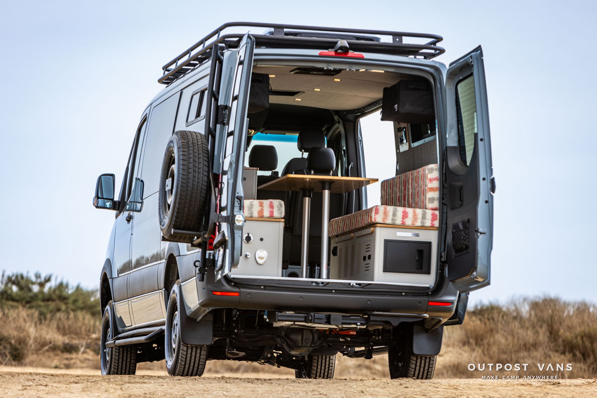 A van with its doors open is parked on a dirt road.