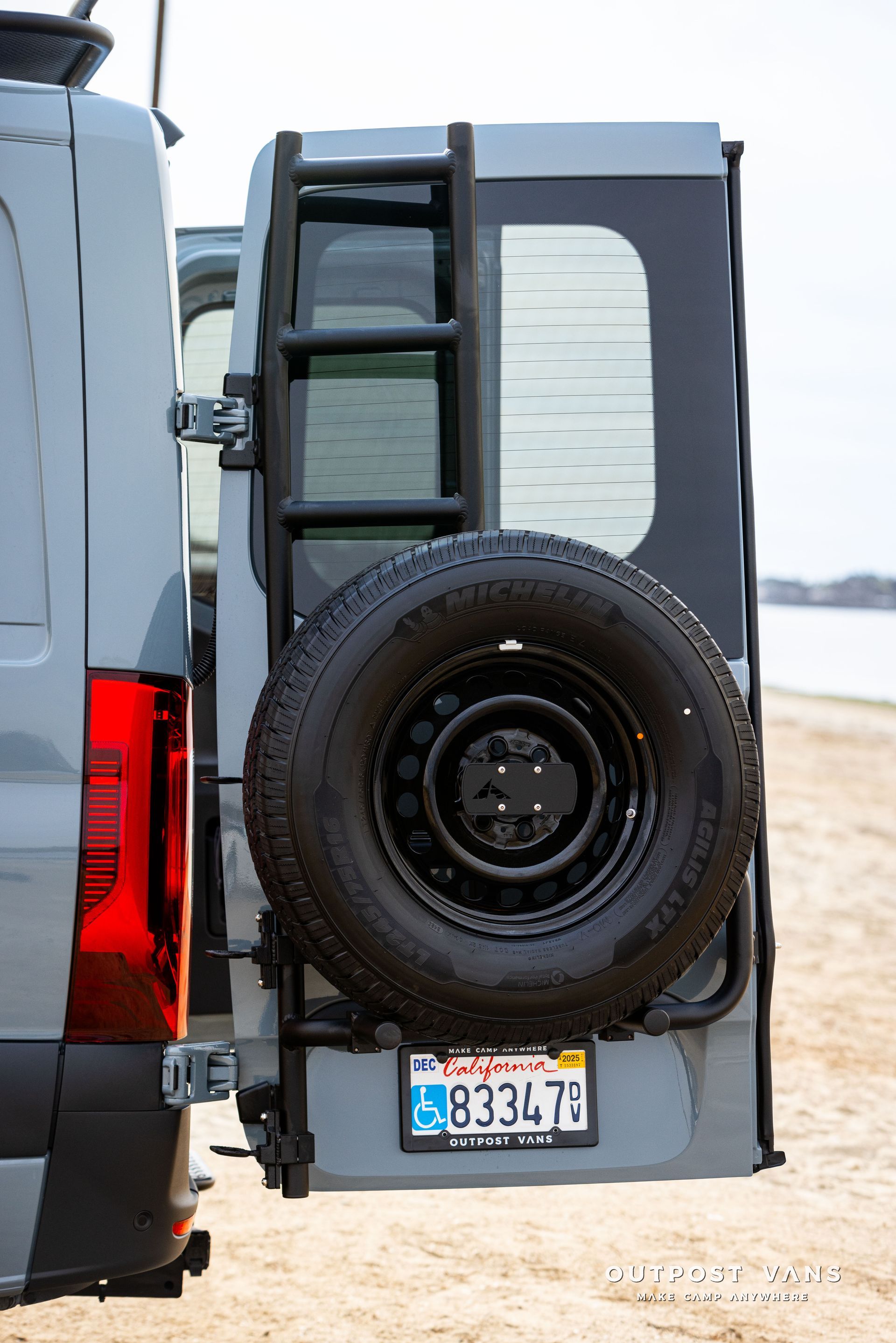 A van with a ladder attached to the back of it and a spare tire.