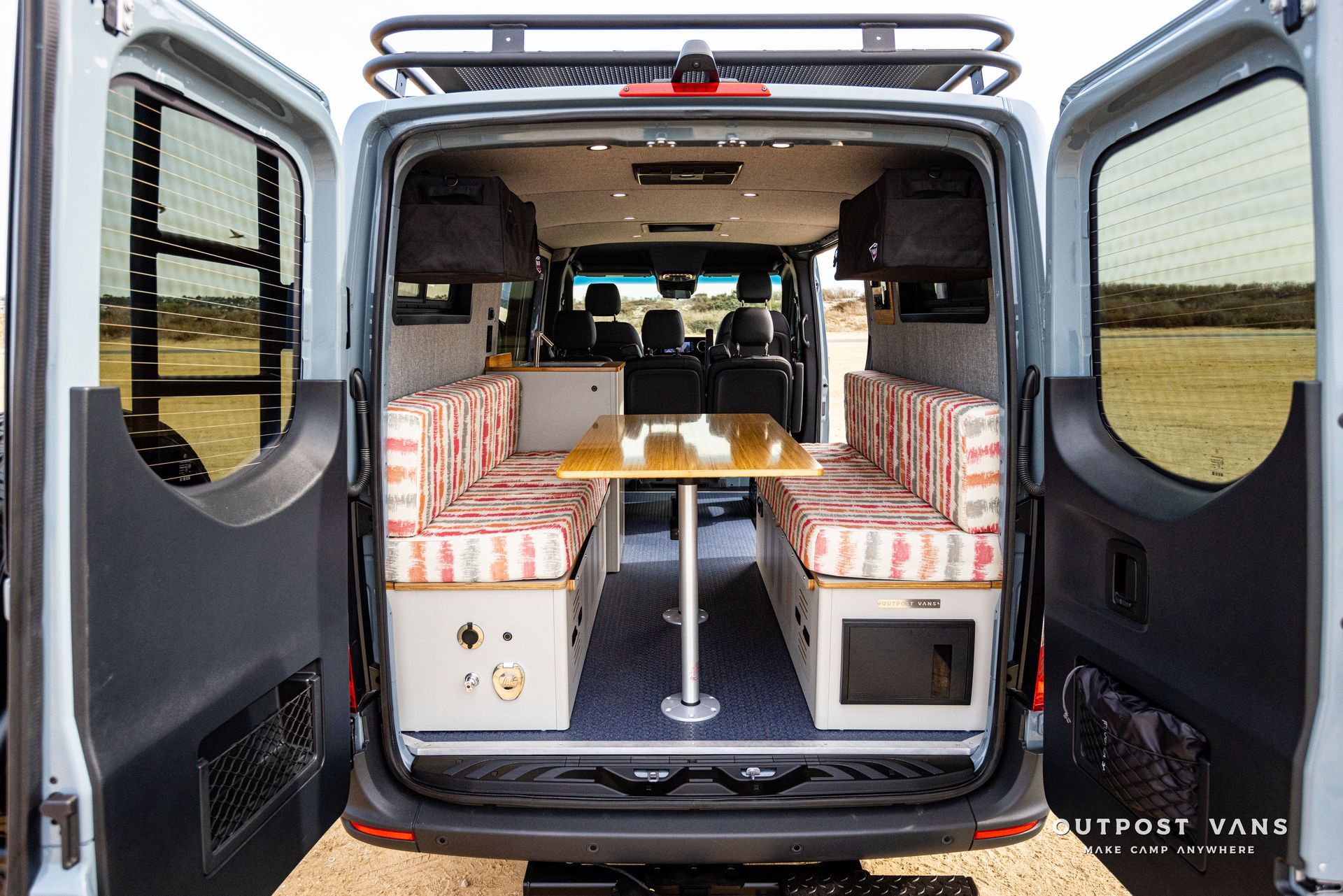 The back of a van with its doors open and a table in the back.