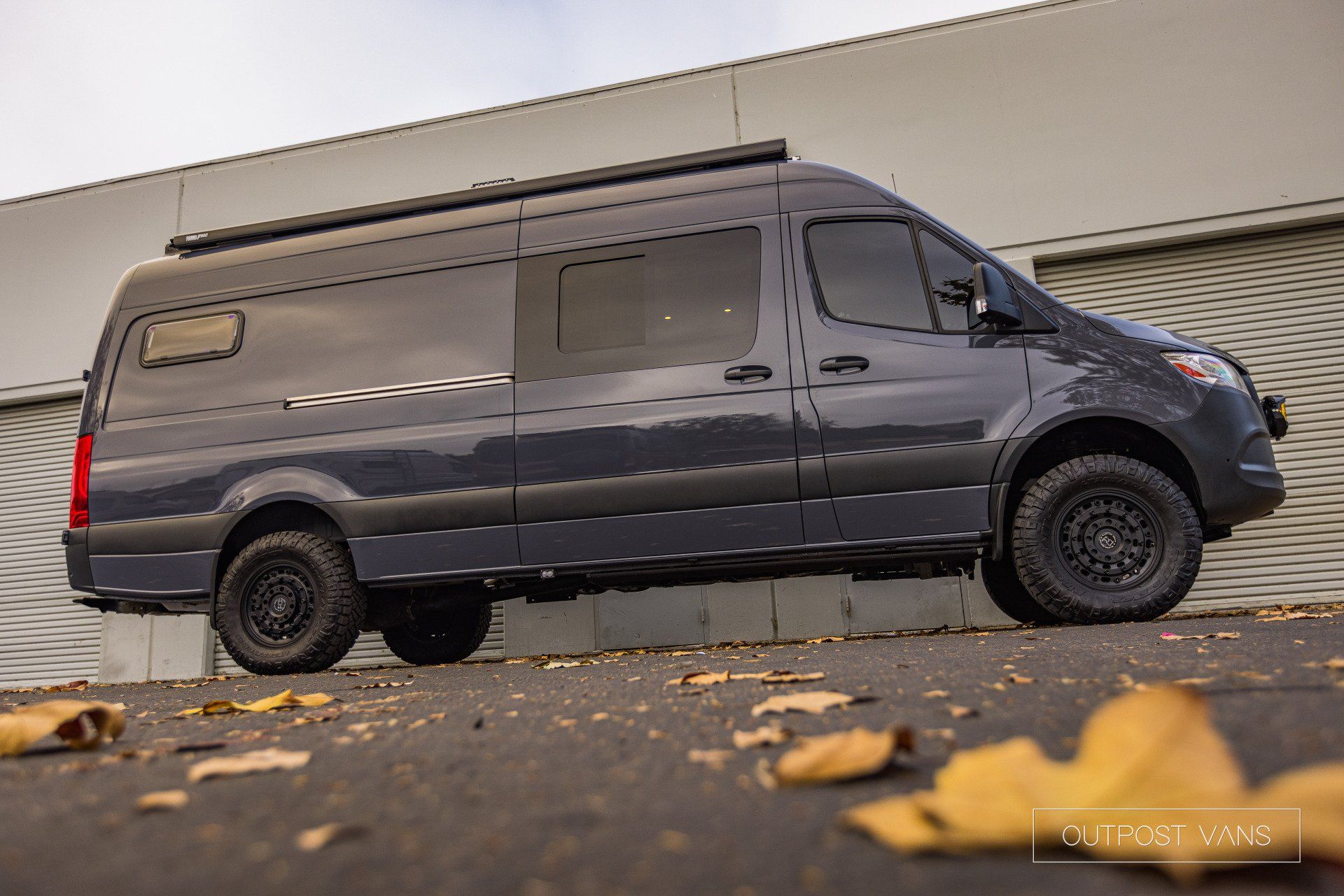 A black van is parked on the side of the road in front of a building.