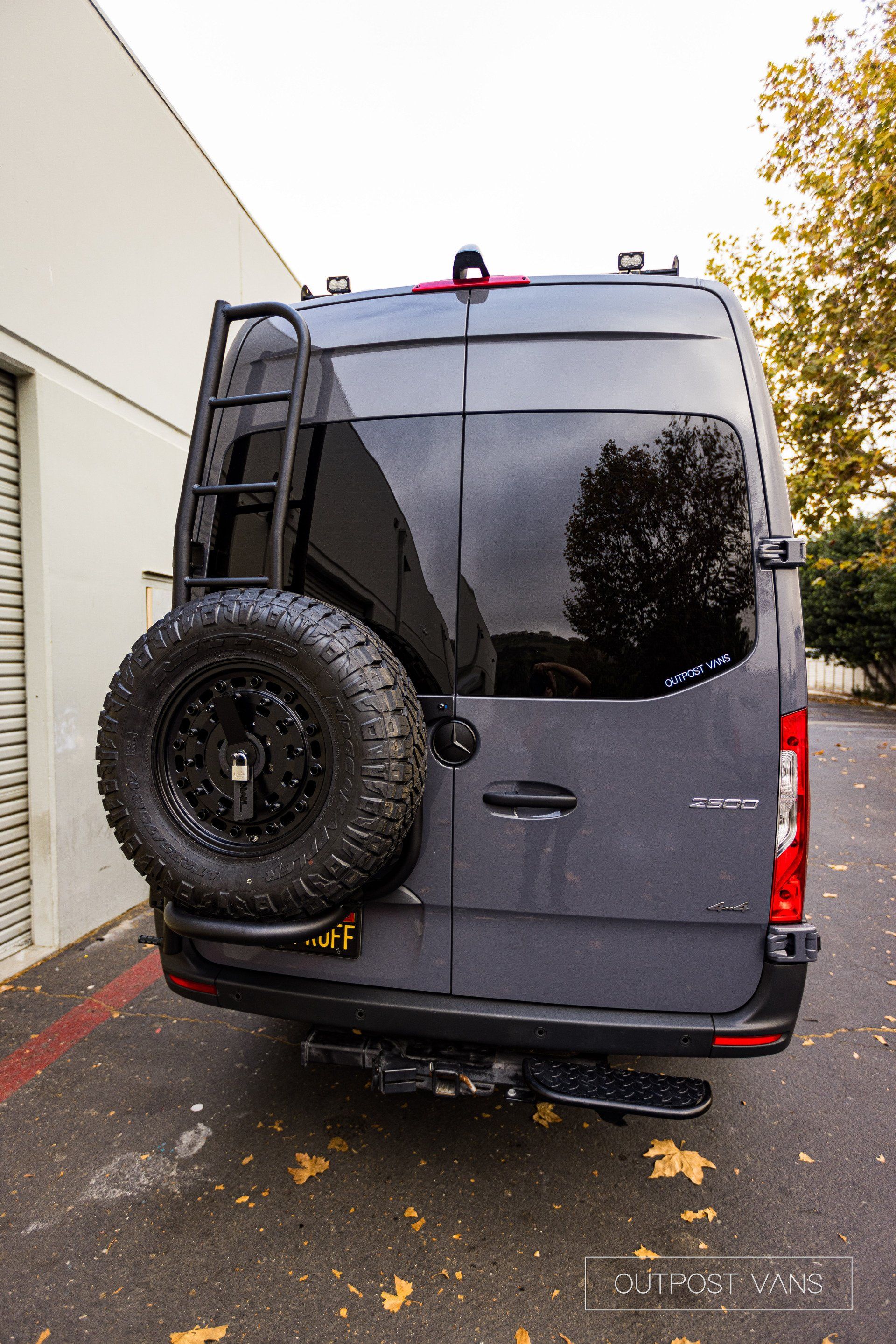 a gray van with a spare tire on the back is parked in front of a building .
