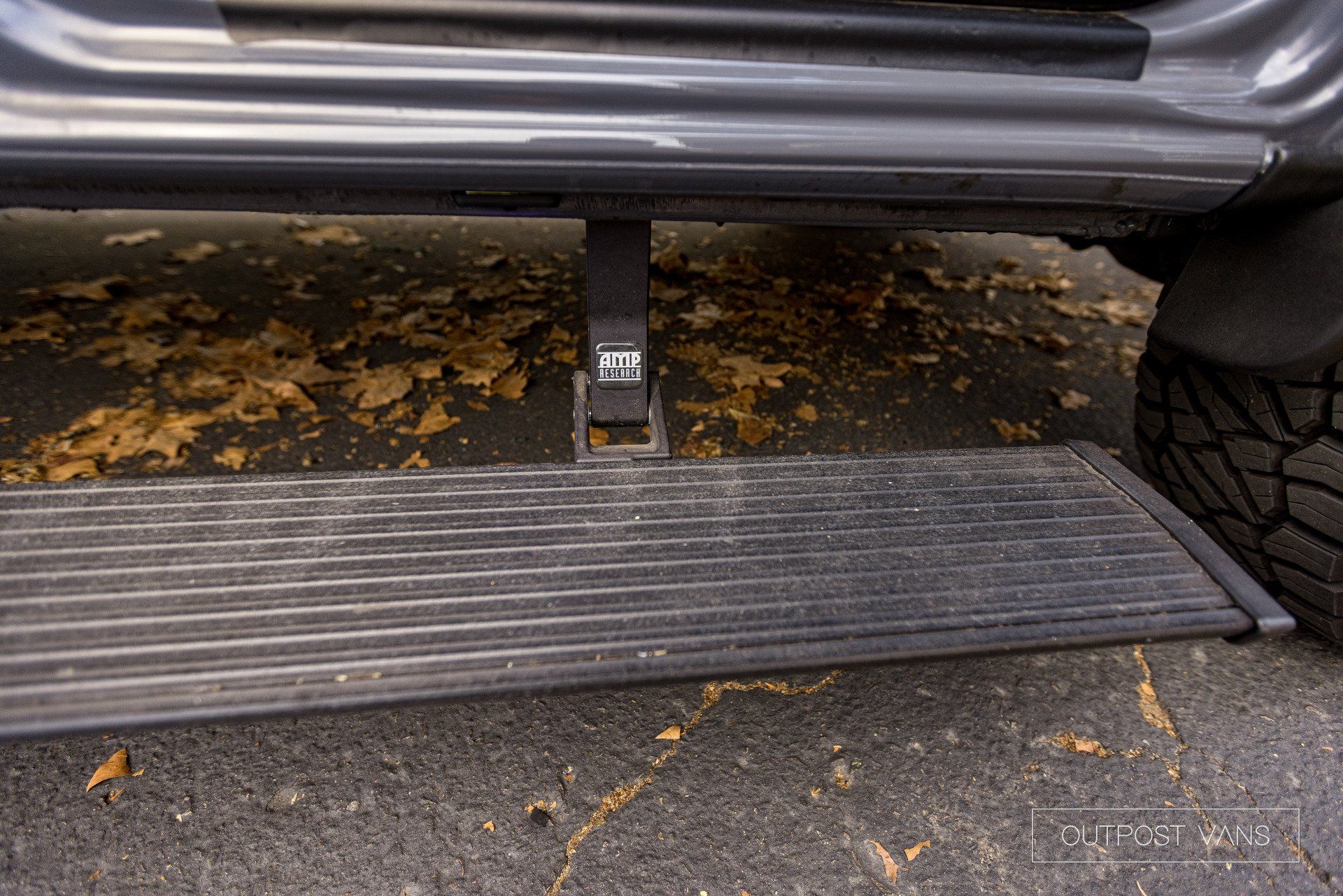 A close up of a car 's side step with leaves on the ground.