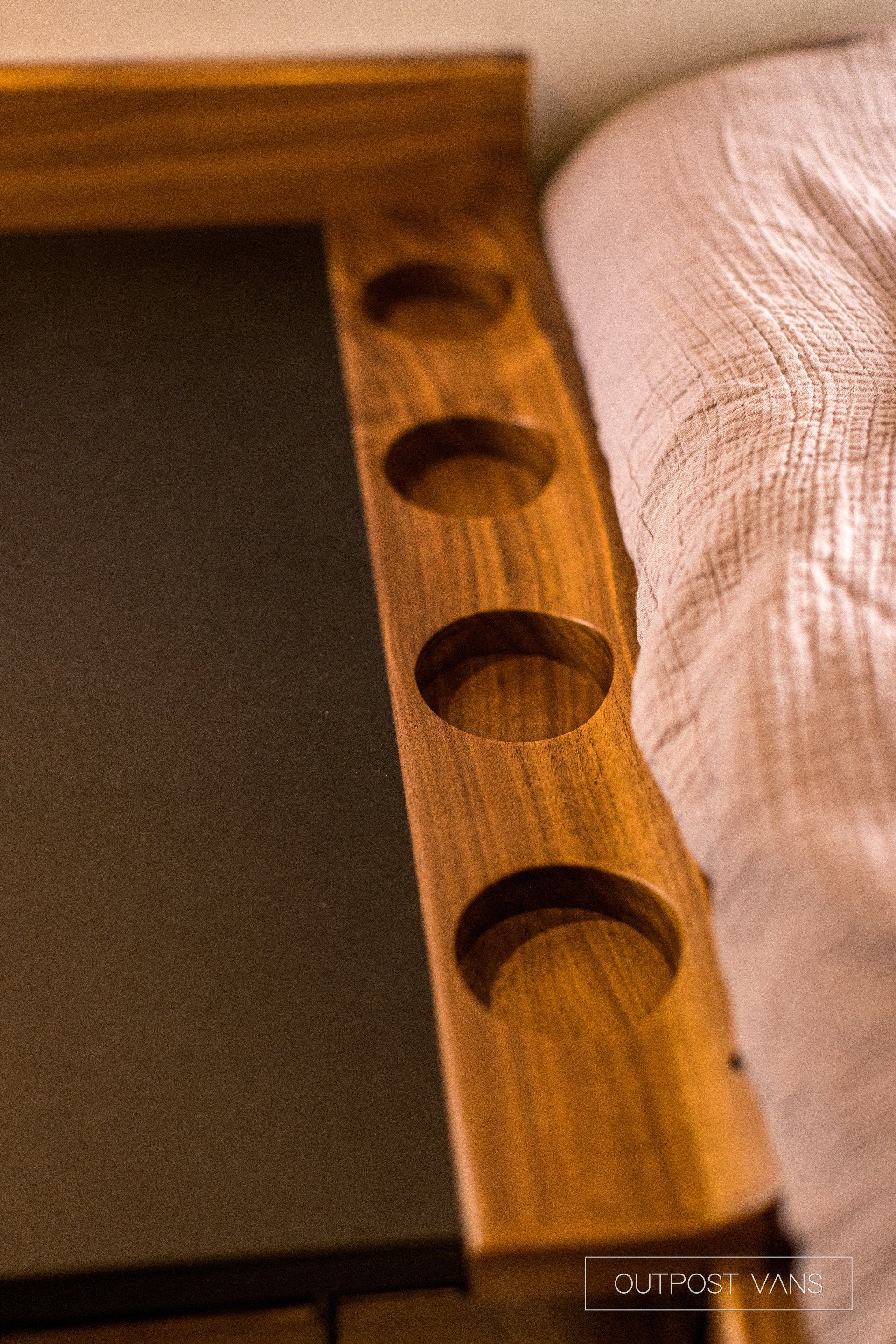A wooden table with holes in it is next to a bed.
