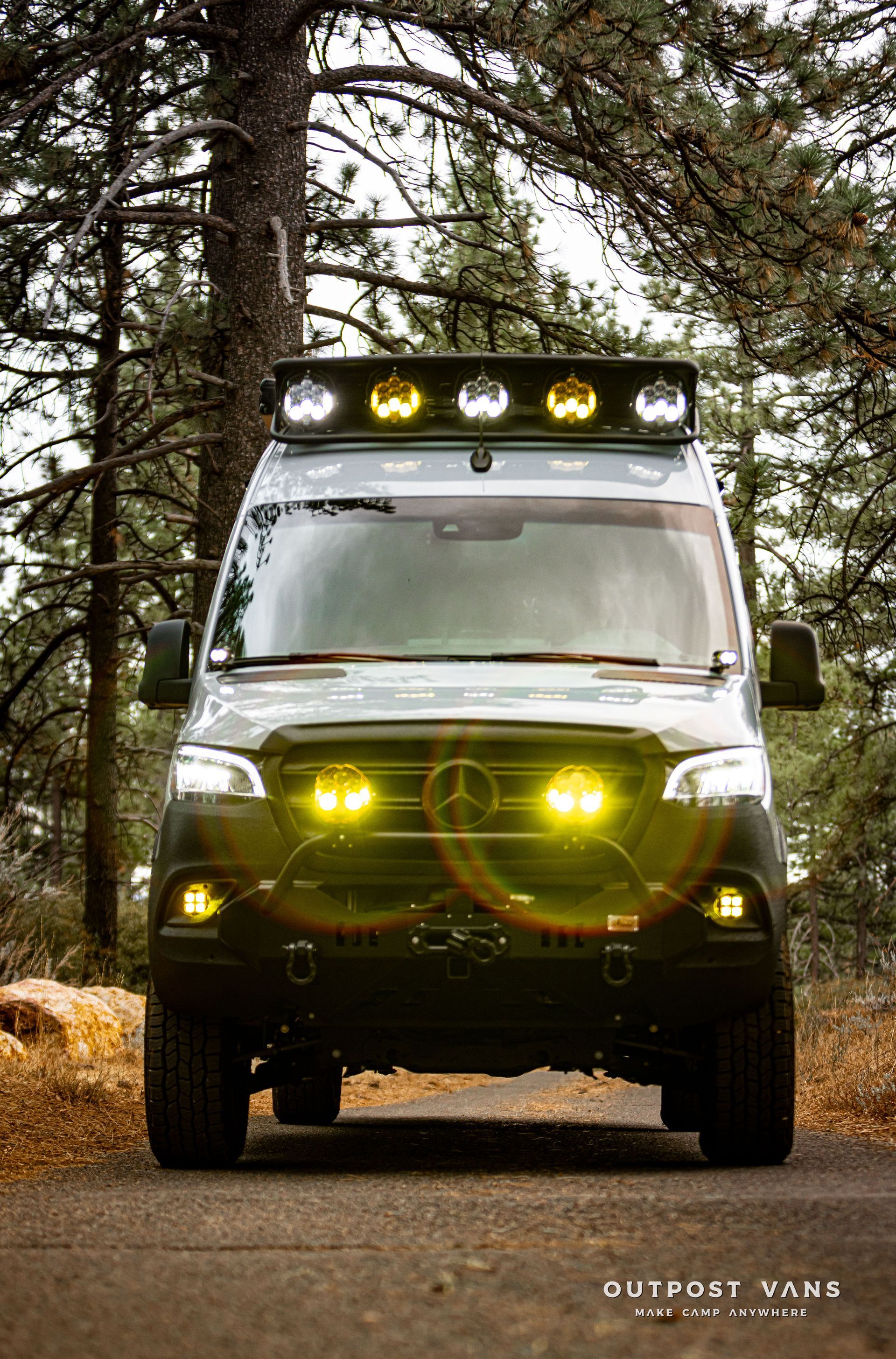 A mercedes sprinter van is parked on the side of a road in the woods.