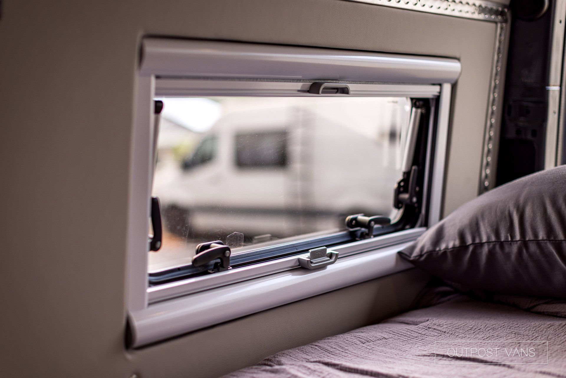 A bed with a pillow and a window in a camper van.
