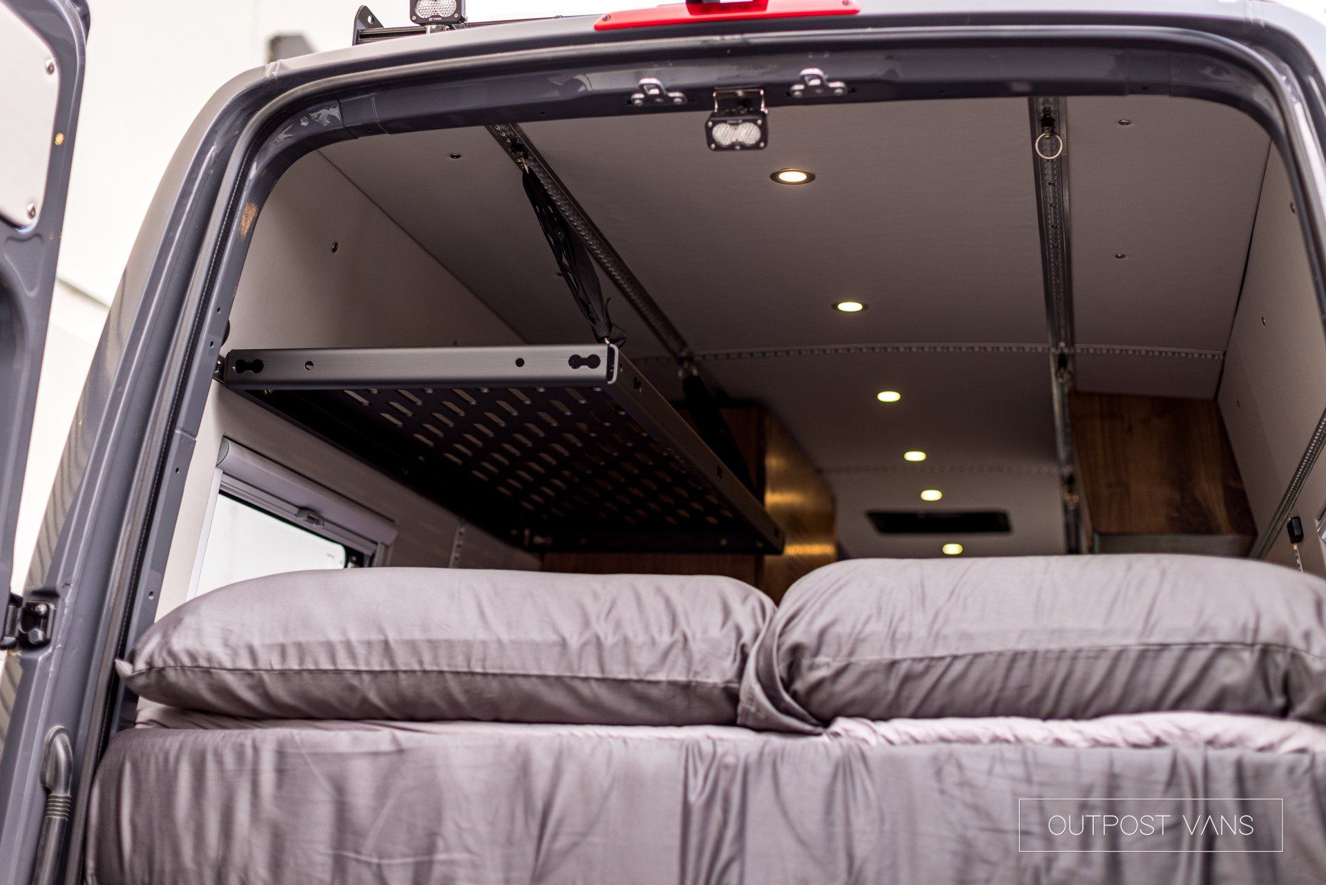 The back of a van with a bed and pillows in it.
